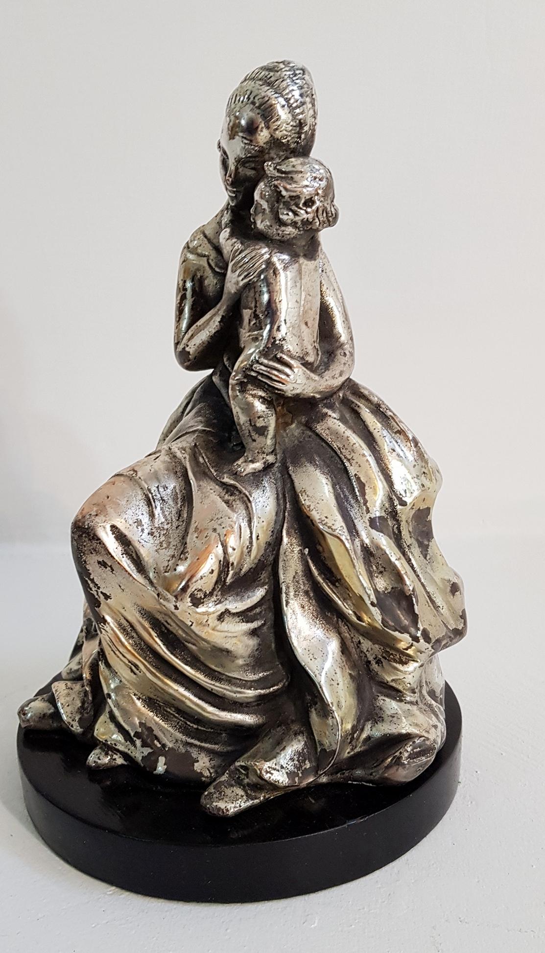 Figurine représentant une mère et un enfant par Guido Cacciapuoti. La figurine repose sur un socle en bois noir et la figurine est fabriquée en terre cuite puis argentée.