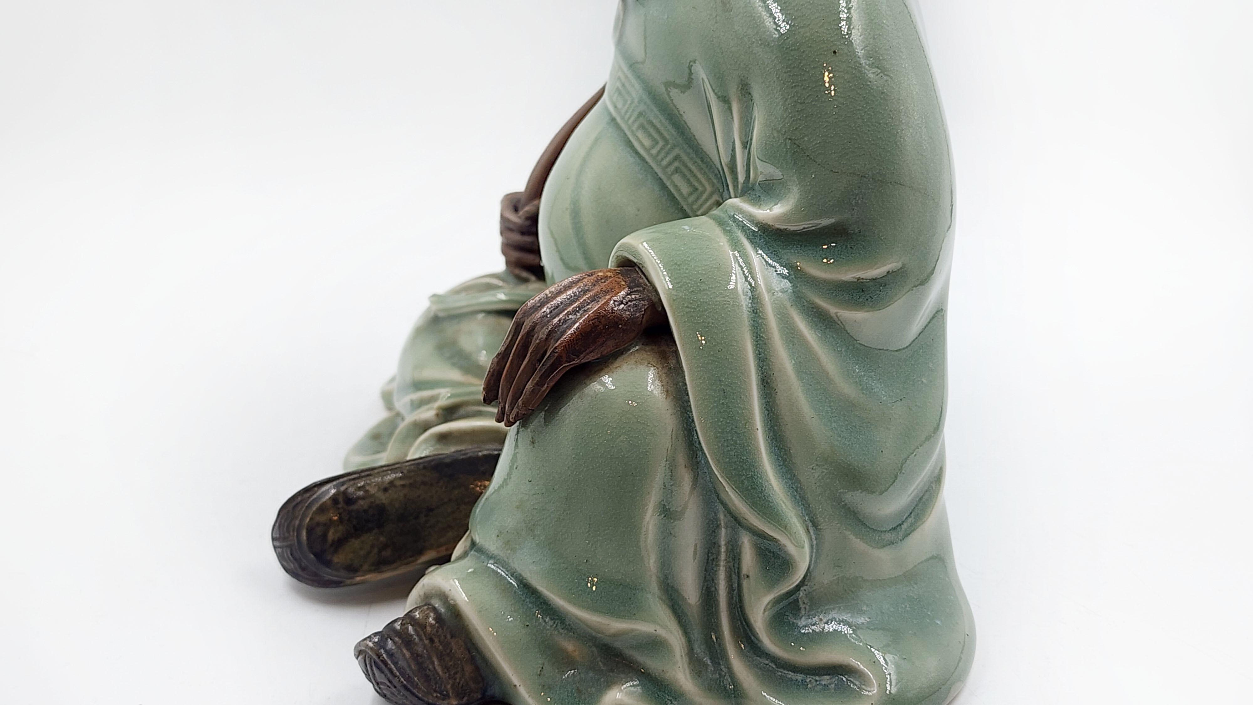 Figurilla, loza Sanda, por Kinkodo Kisuke, periodo Edo, cerámica, vidriado celadón
Esta pieza de cerámica representa a un hombre sentado con expresión serena, vestido con una túnica verde celadón pálido. La figura sostiene un bastón rústico en la