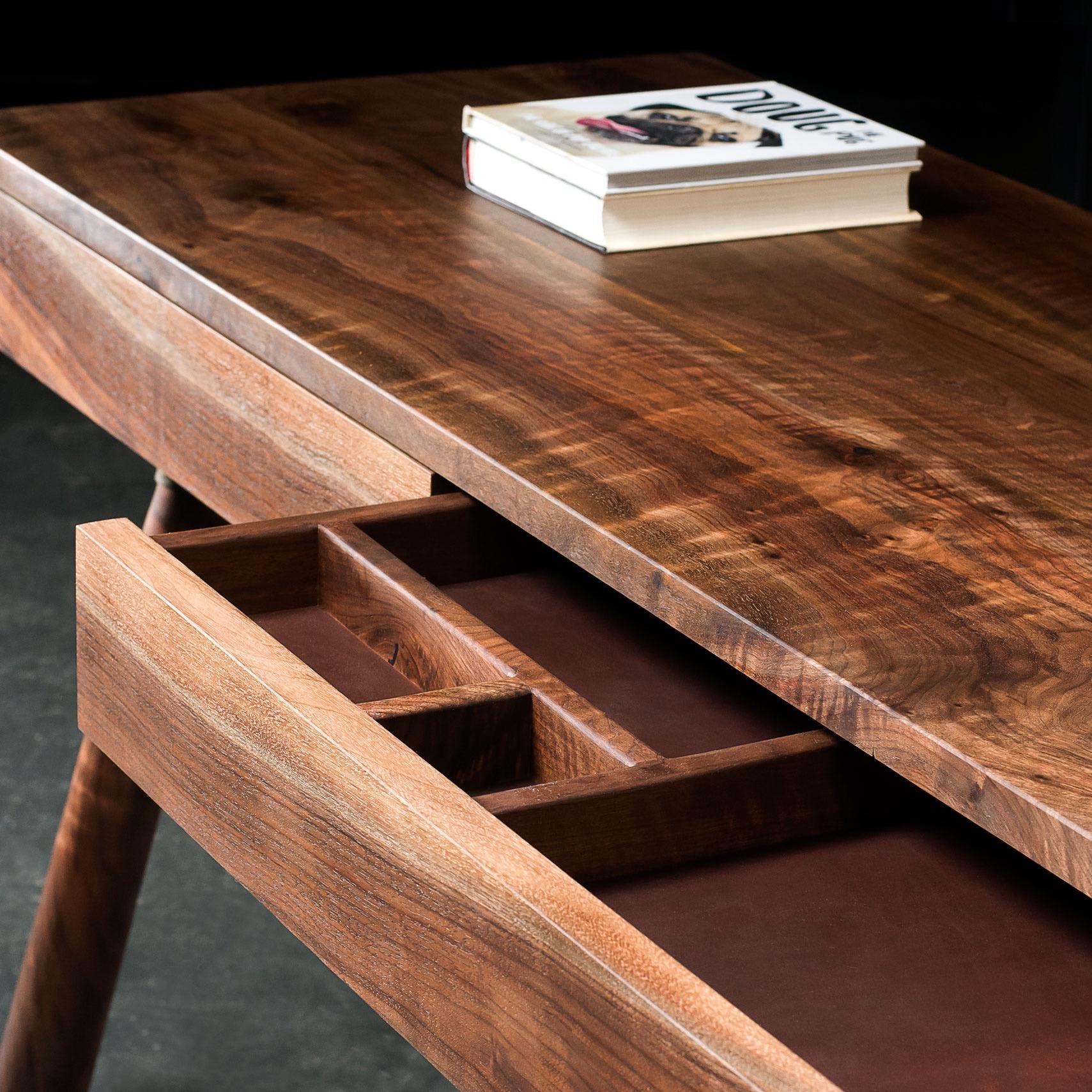 FIJN desk is handcrafted in solid wood. Shown here in figured Oregon black walnut. Solid wood drawers are lined in leather and inserts can be customized to suit.

Hand-turned legs attach to the desk top in steel cuffs. 

As shown: 60” L x 24” W.