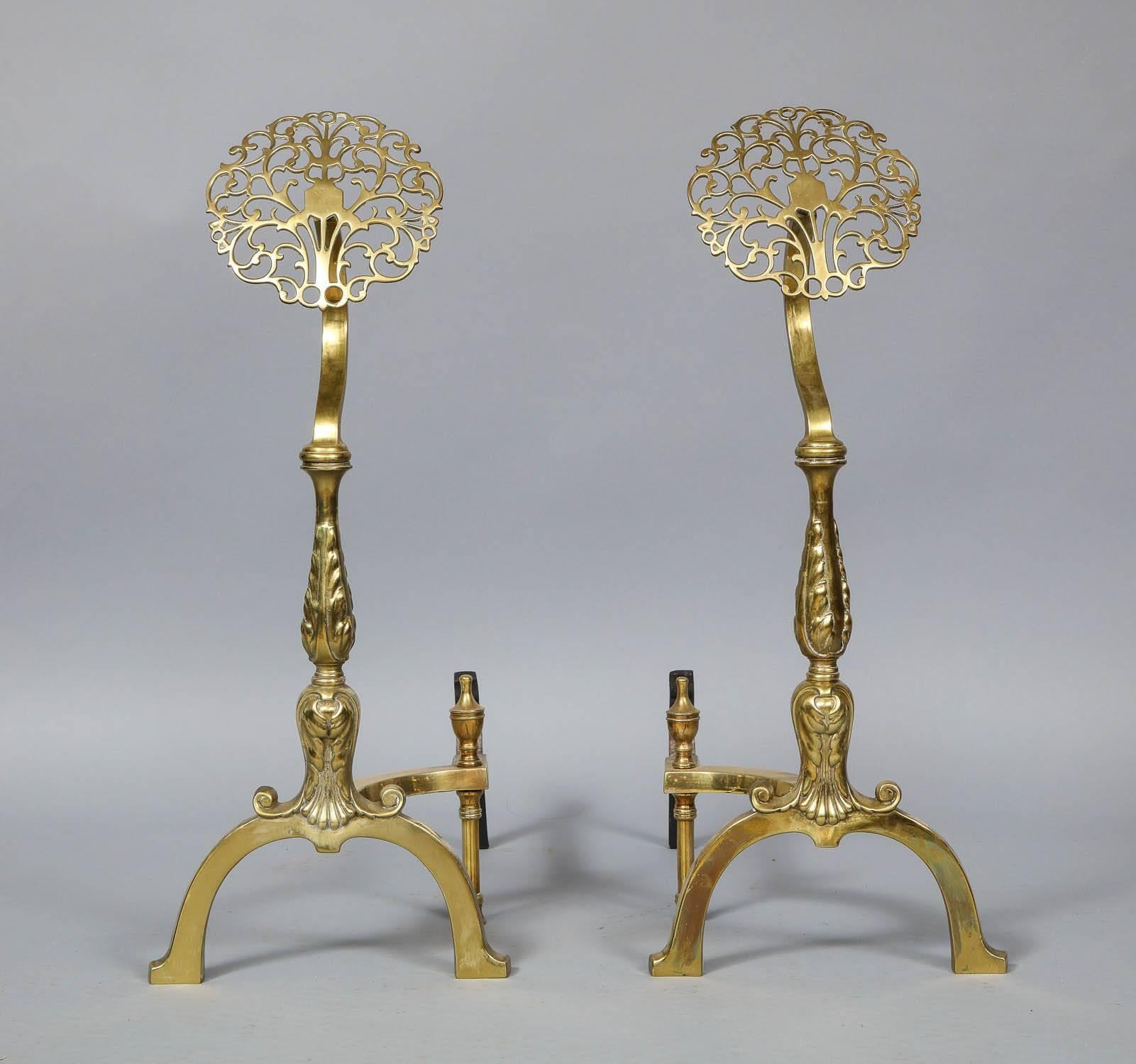 A pair of striking andirons with round brass filigree heads poised on decorated brass shafts on arched legs with capped brass returns surmounted by urn finials.