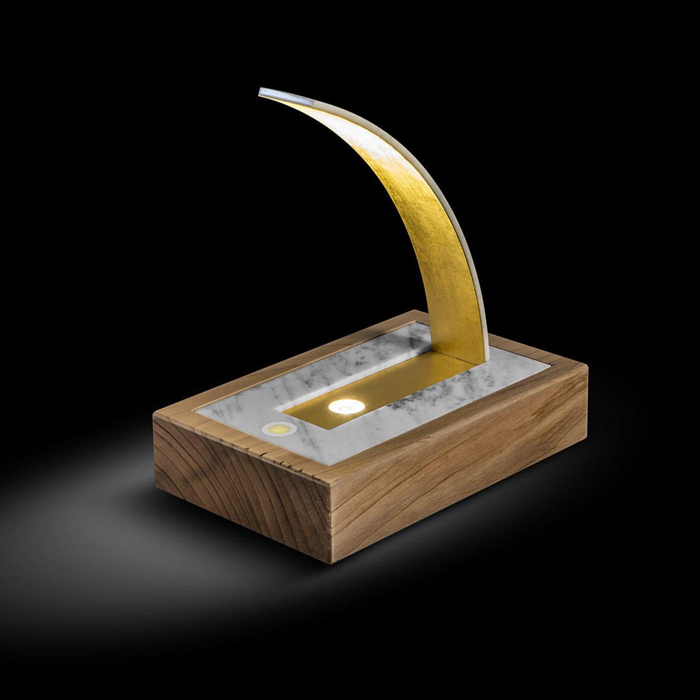 This table lamp is characterized by a sculptural silhouette composed of an elegant combination of refined materials. The rectangular base is composed of an external frame made of solid Lebanon cedar wood and an internal base made of Carrara Gold