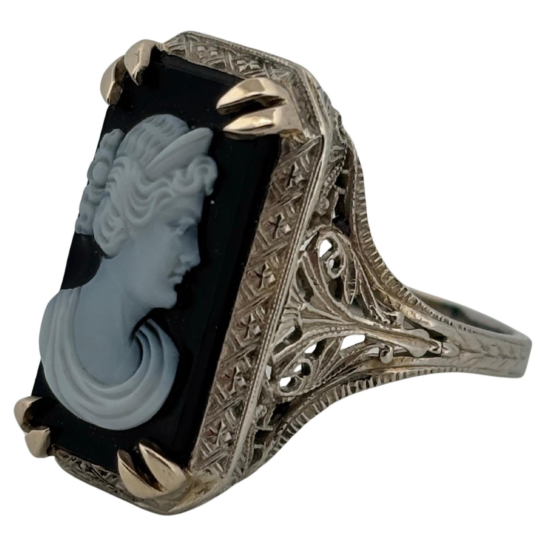 Questo squisito anello in filigrana d'oro bianco 18 carati presenta un cammeo in onice nero finemente intagliato che raffigura il profilo di una donna classica. Il cammeo centrale misura 11,75 mm di lunghezza per 9,00 mm di larghezza, offrendo un