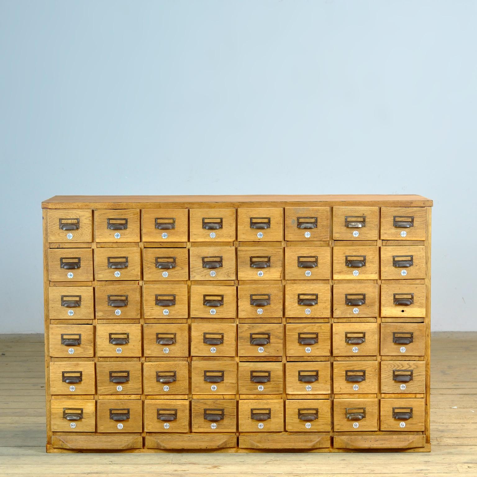This filing cabinet was made in Germany around the 1930s from oak and pine. It has 48 drawers with metal handles. Originally, this was the top part of a cabinet, which explains the pull-out shelves at the bottom. The internal dimensions of the
