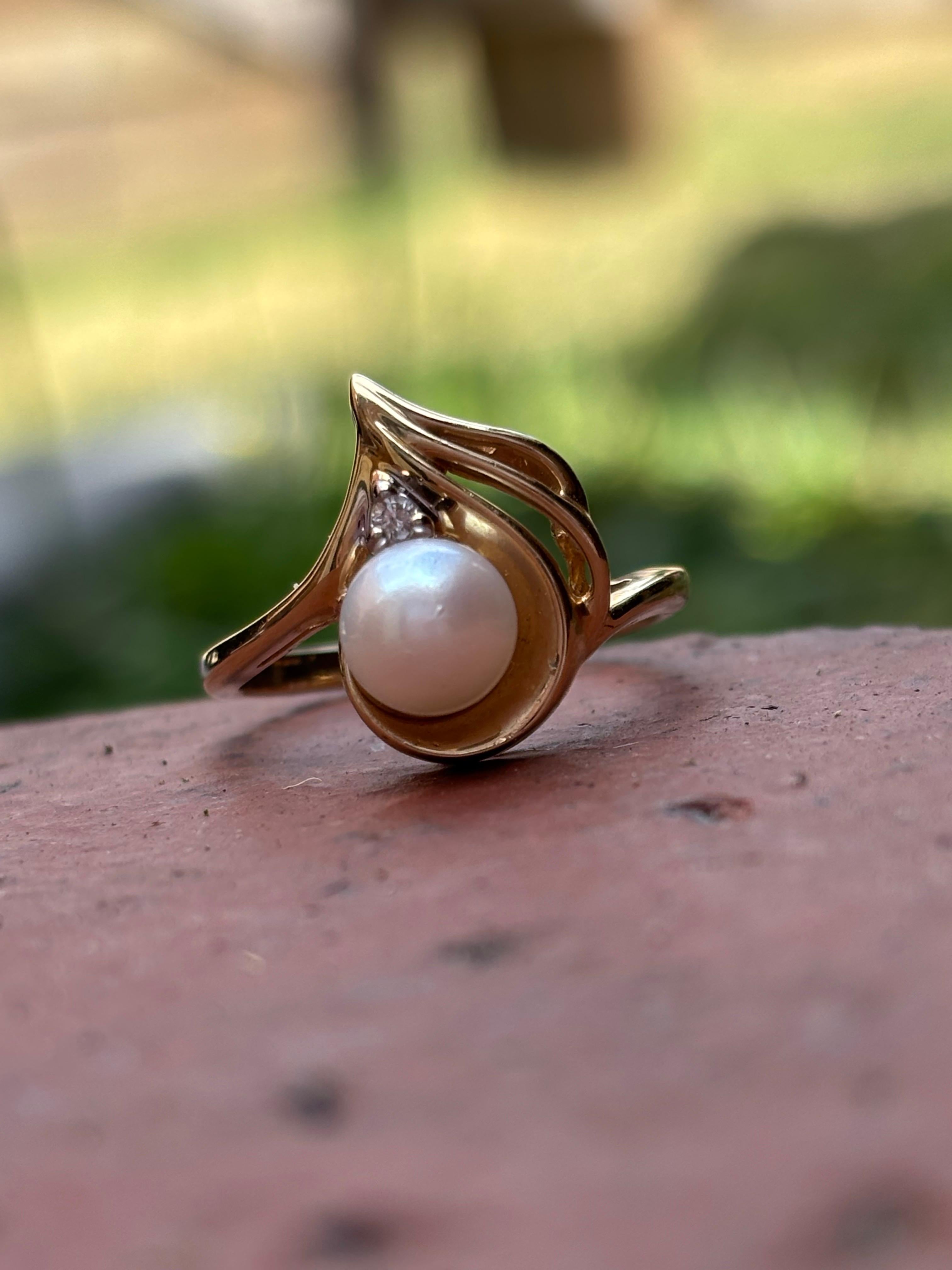 Cette élégante bague vintage est réalisée en or jaune 14 carats et présente un gracieux motif tourbillonnant qui évoque une sophistication intemporelle. En son centre repose une perle d'eau douce lumineuse de 6,5 mm, prisée pour son éclat crémeux et