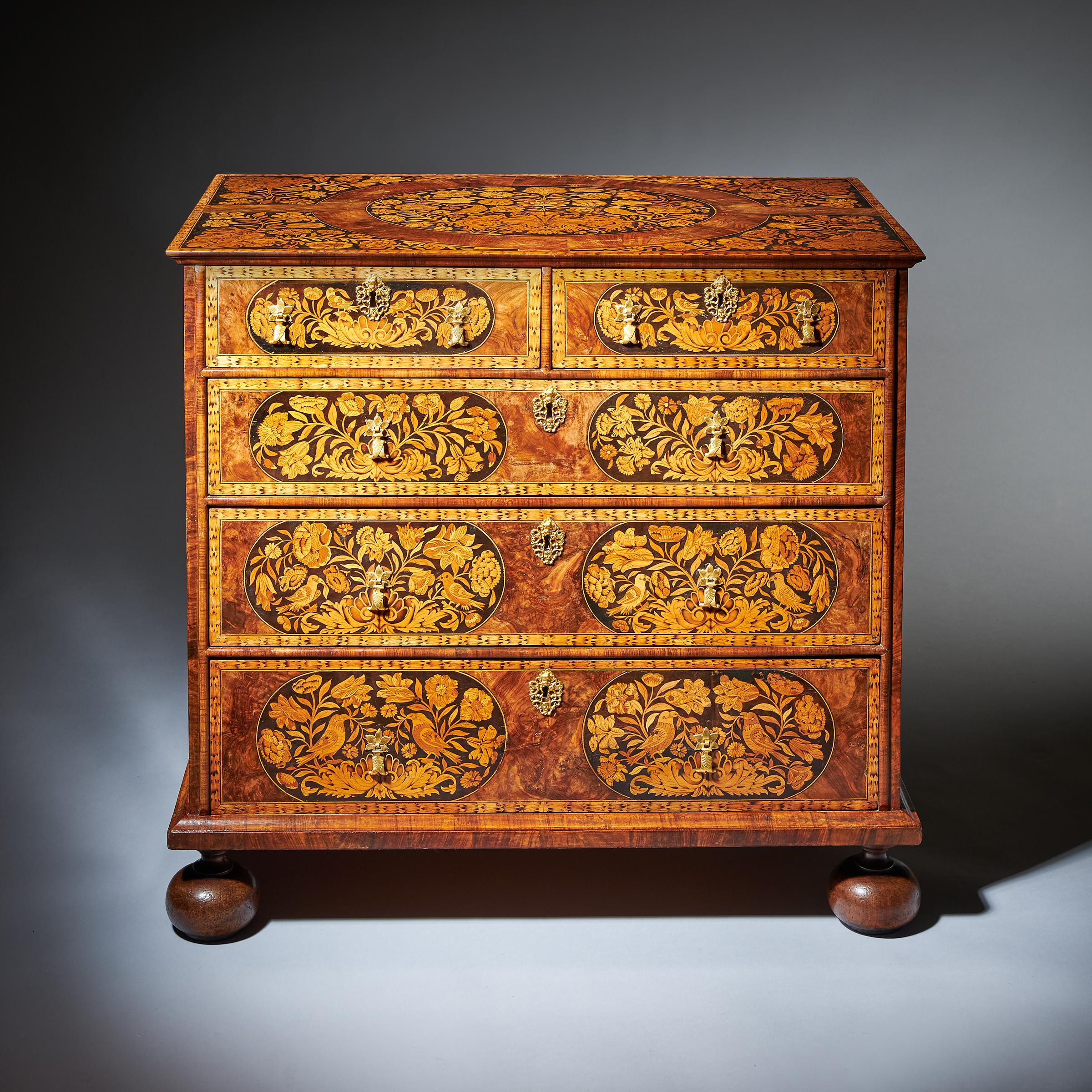 A William and Mary walnut floral marquetry chest, circa 1690.

The rectangular ogee moulded top with a central banded oval inlaid with spring flowers, birds and scrolls of acanthus, on an ebony ground. 

The two short over three long oak-lined