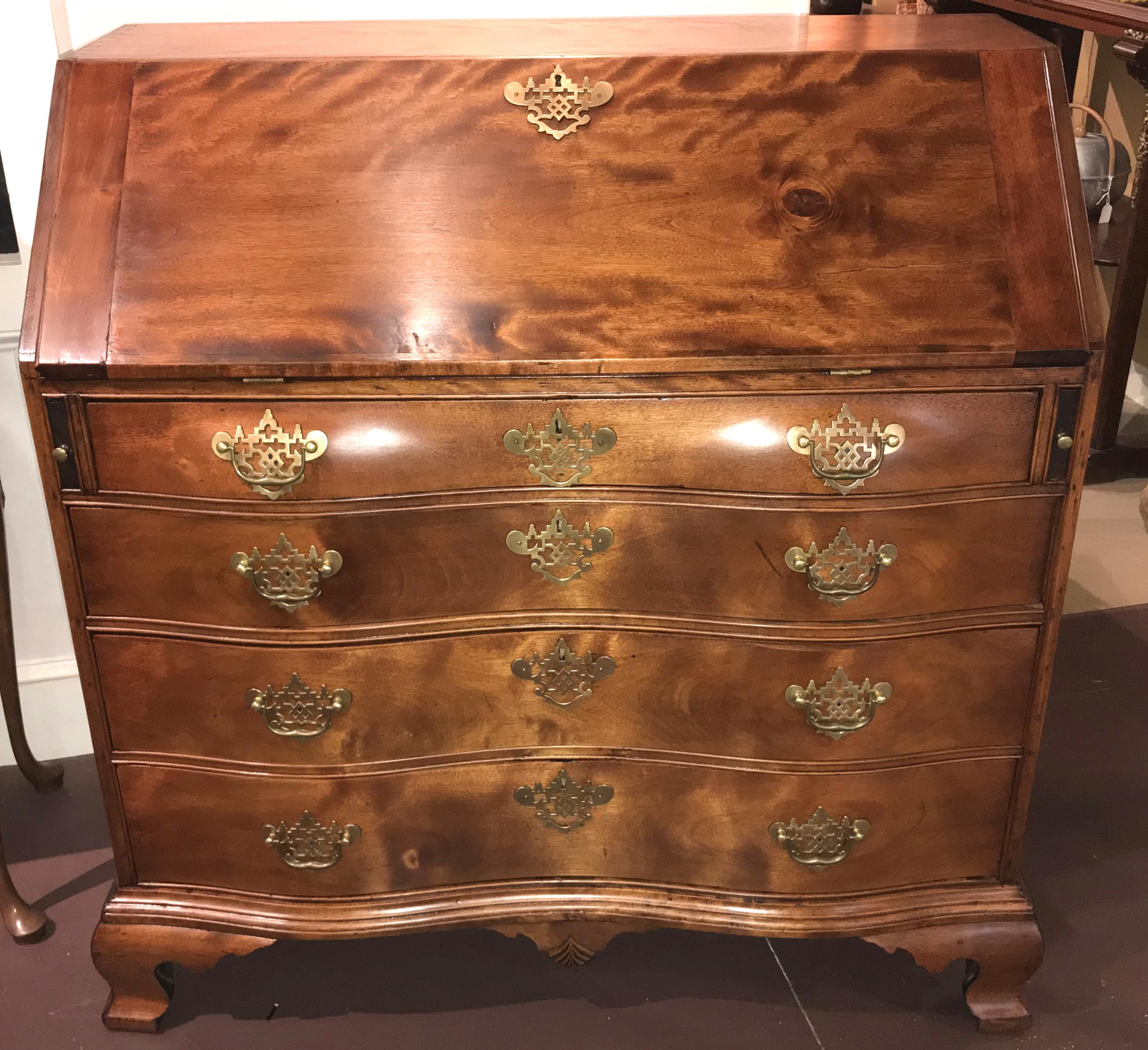 A fine 18th century American oxbow form slant front desk in flame birch with a compartmentalized interior featuring three radial fan carved drawer fronts and four valanced open cubbies, surmounting two graduated rows of fitted drawers of various
