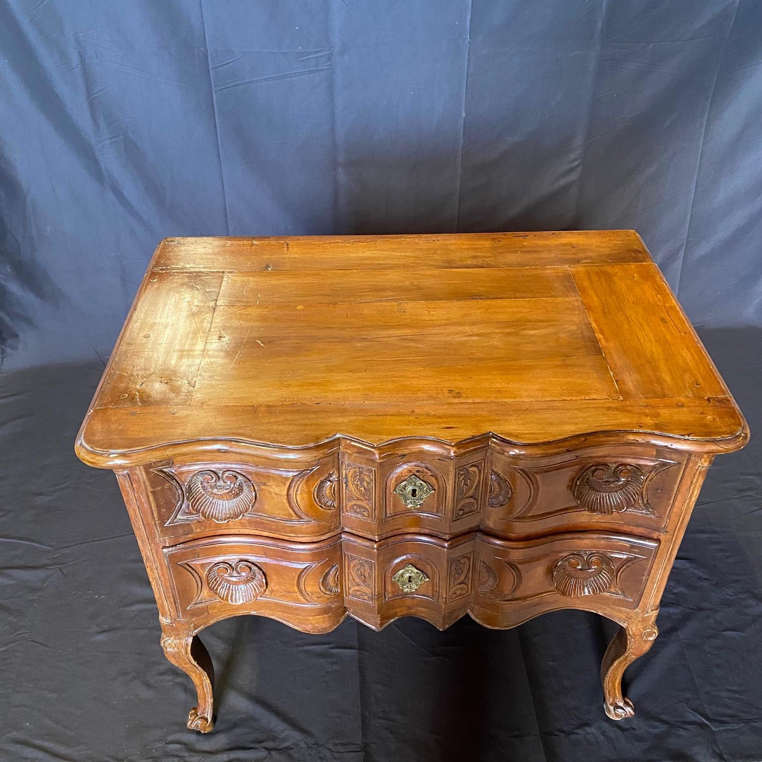 Elegante commode francese in noce intagliato a mano risalente al XVIII secolo, caratterizzato da un fronte increspato intagliato e da tiranti a conchiglia che fanno parte del corpo.   Il corpo, intricatamente intagliato, presenta due ampi cassetti,