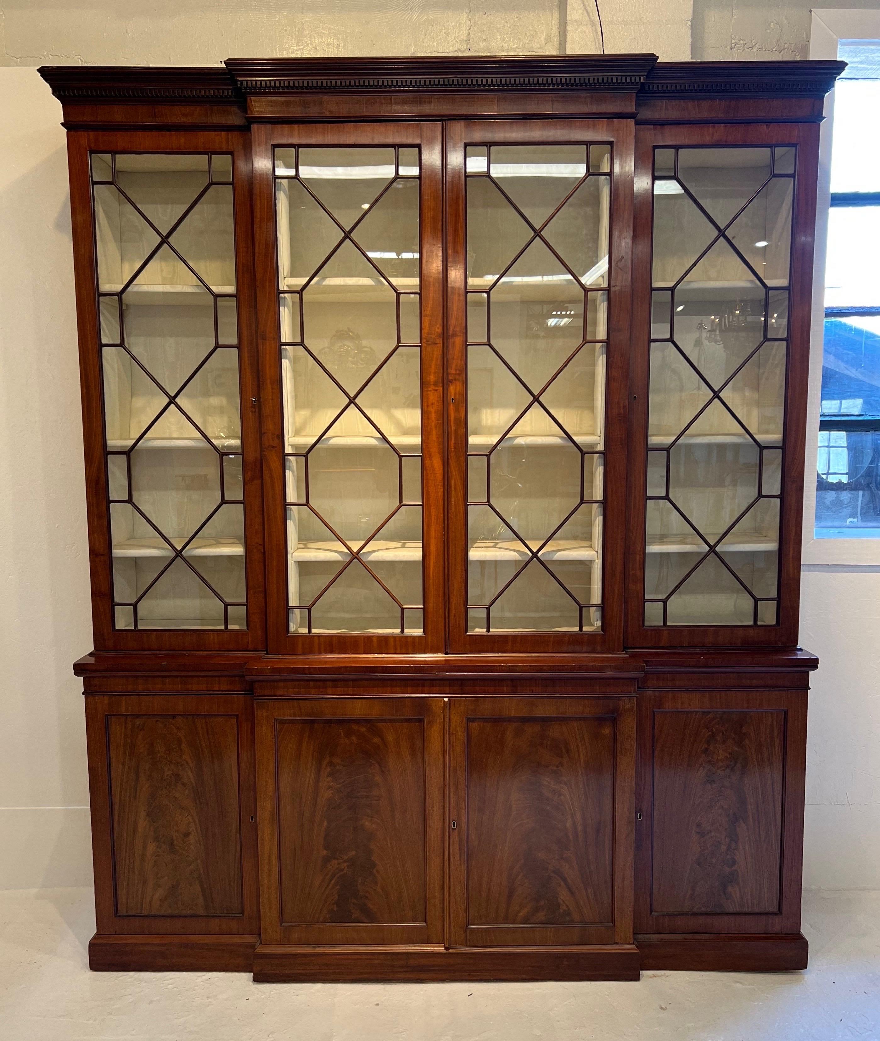 Fine 18th century Georgian mahogany breakfront bookcase on a plinth base with linen slides in the base and lined interior seem behind the glazed doors of the top. Warm color with highly figured panels. Interior lighting has been added when the silk