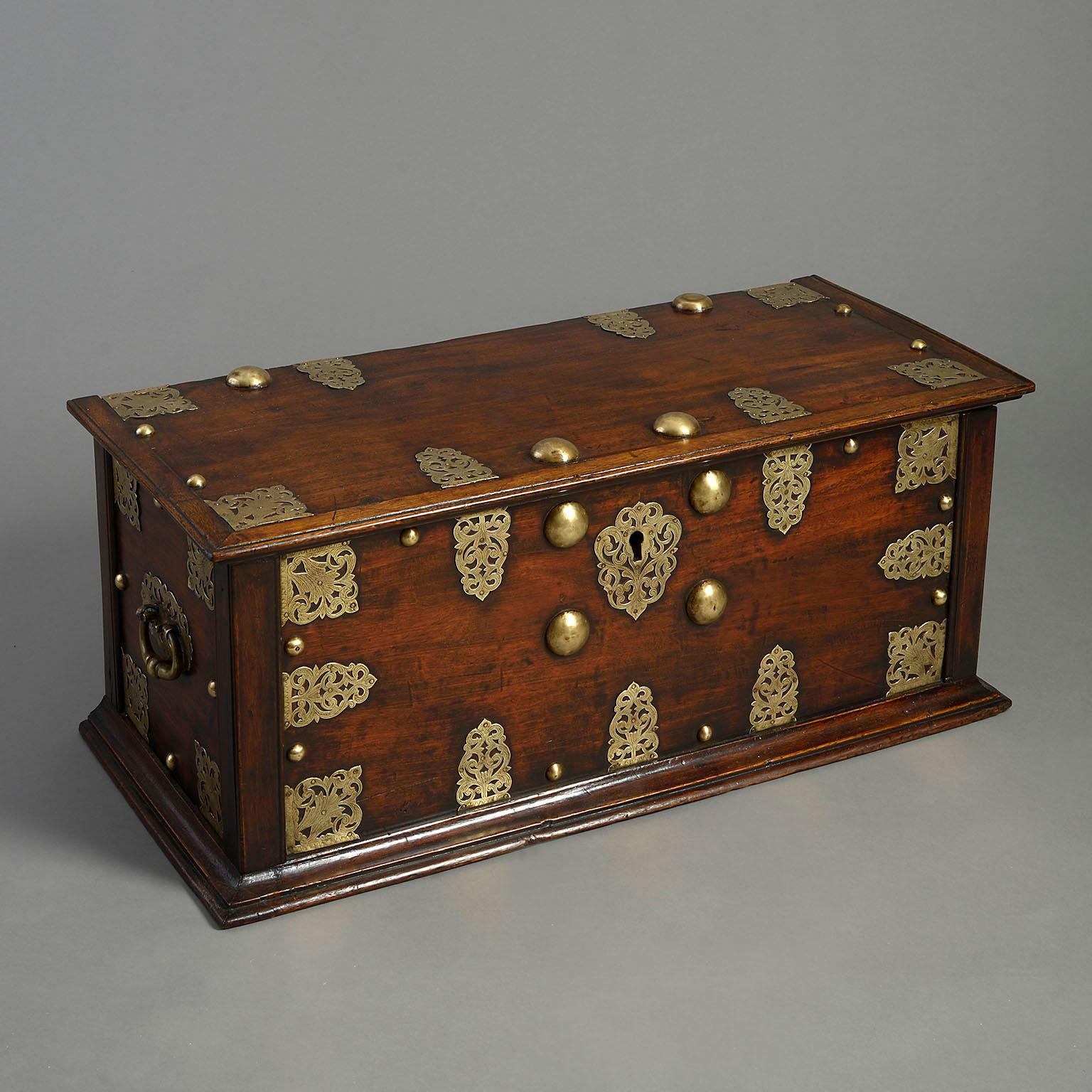 An 18th century hardwood and brass mounted chest, the iron-hinged top, sides and front decorated with pierced foliate mounts and studs, with carrying handles at either end.