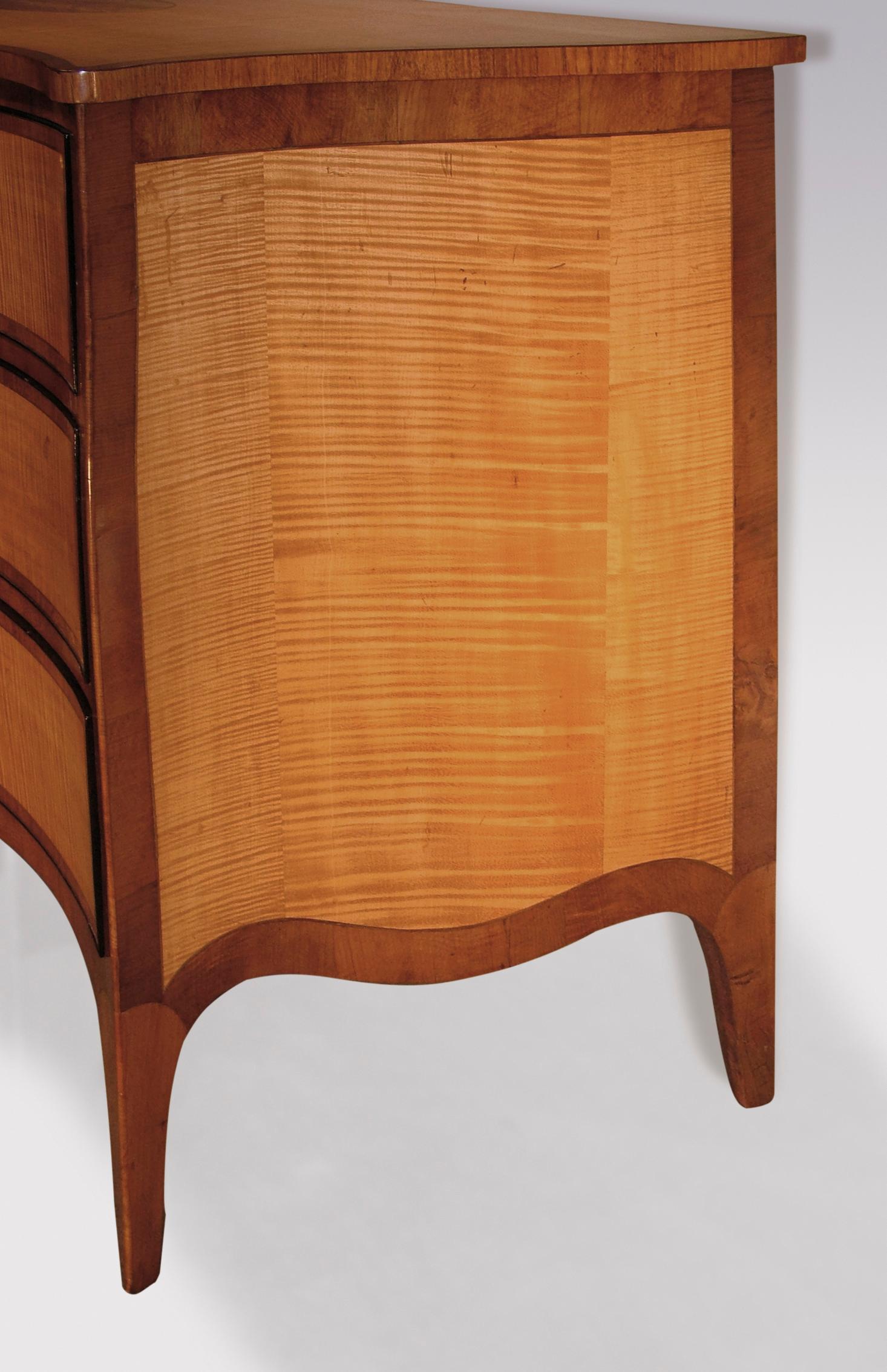 Une belle commode en bois de lièvre de la fin du 18e siècle de la période Hepplewhite, en buis vert cordé et en bois de padouk croisé, ayant un dessus serpentin avec un panneau central ovale incrusté en bois de padouk, au-dessus de trois tiroirs en