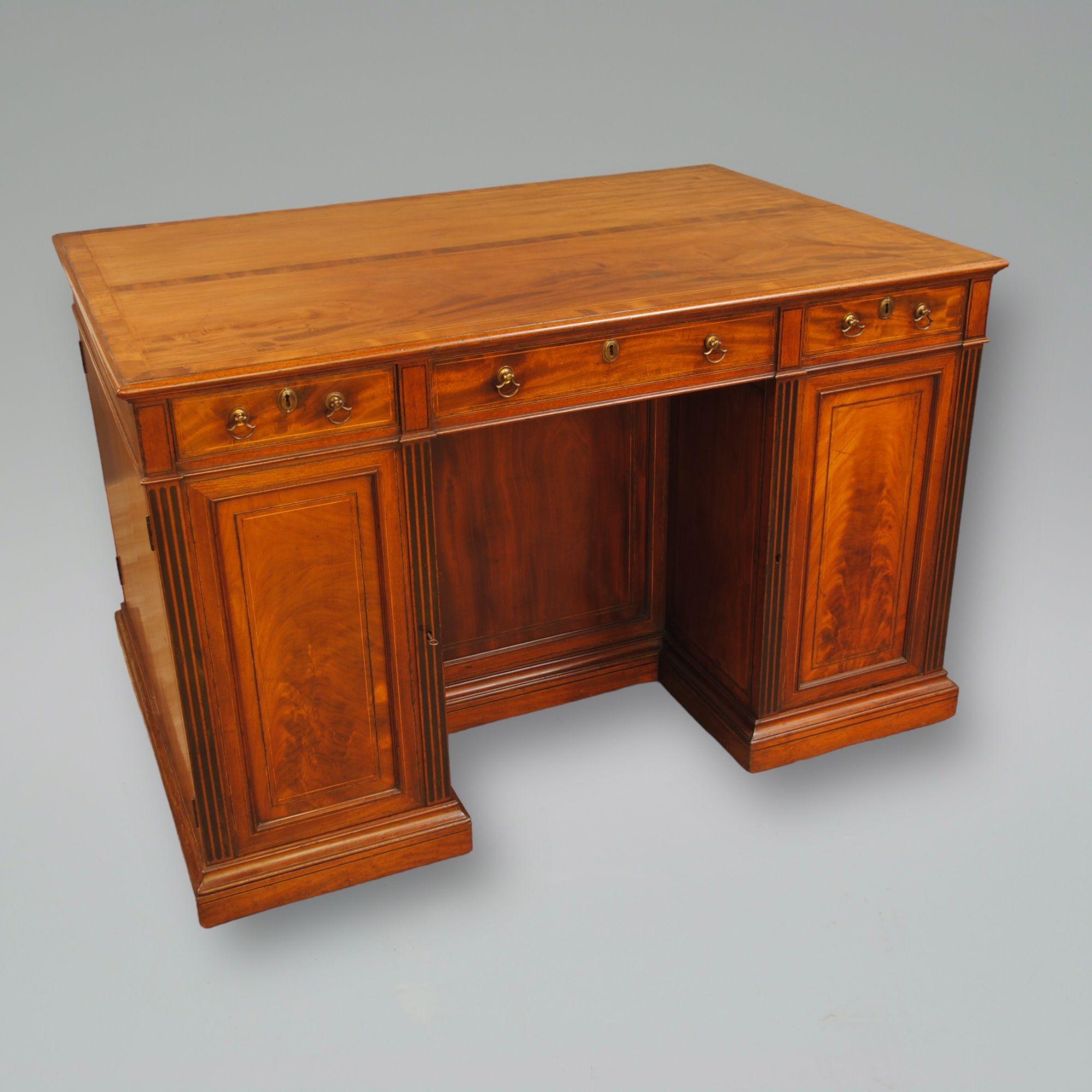 A fine quality late 18th century mahogany free standing library desk, the flame mahogany cupboards with ebony fluting to the sides of the kneehole, are fitted with drawers. The veneered top is cross banded and strung in boxwood. The other side has