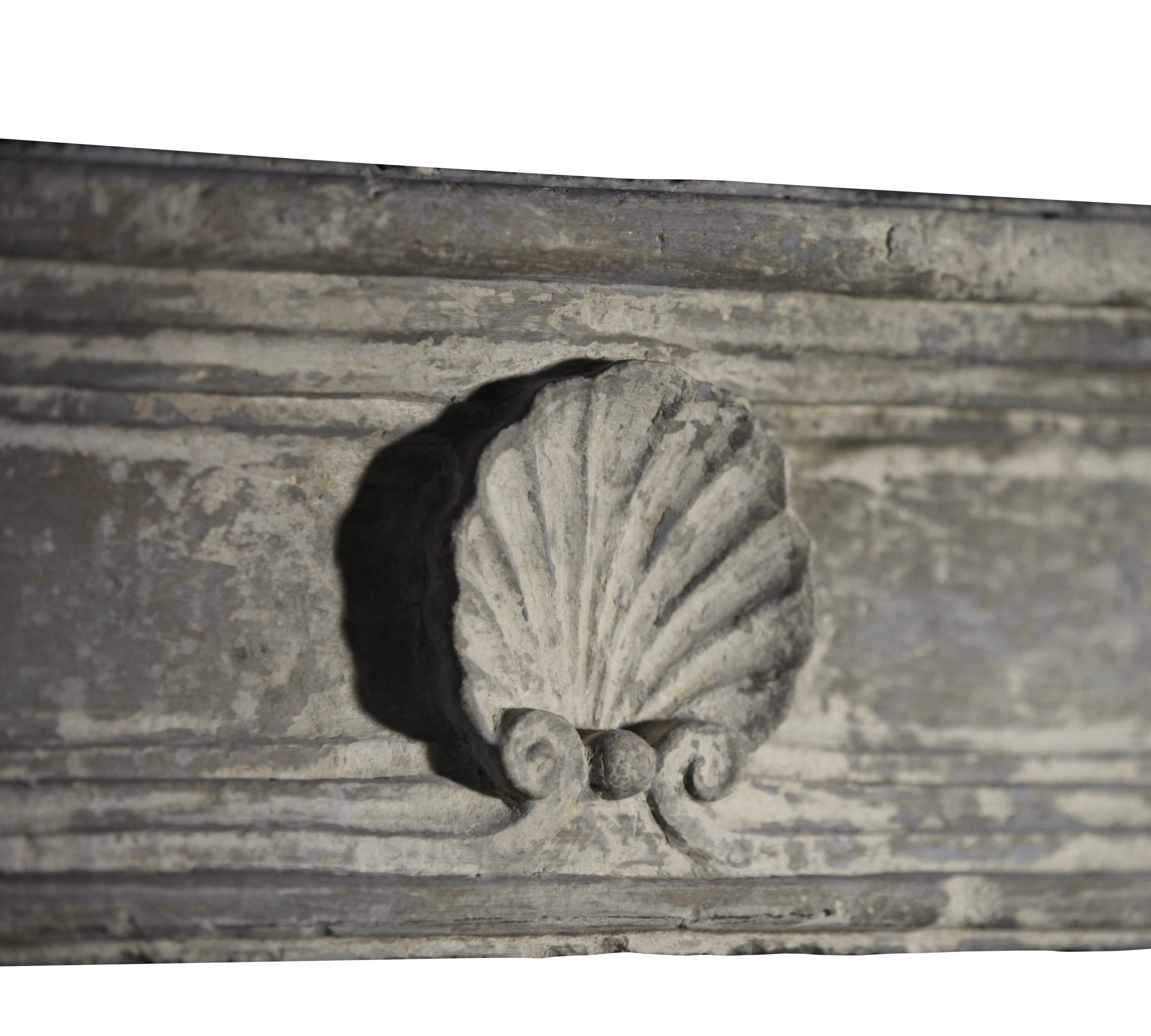 This is very small French country limestone fireplace surround from the Louis XV period. A delicate surround with great authentic patina and which was installed in a wood pannel room from the 18th century. A beautiful scallop in the center of the