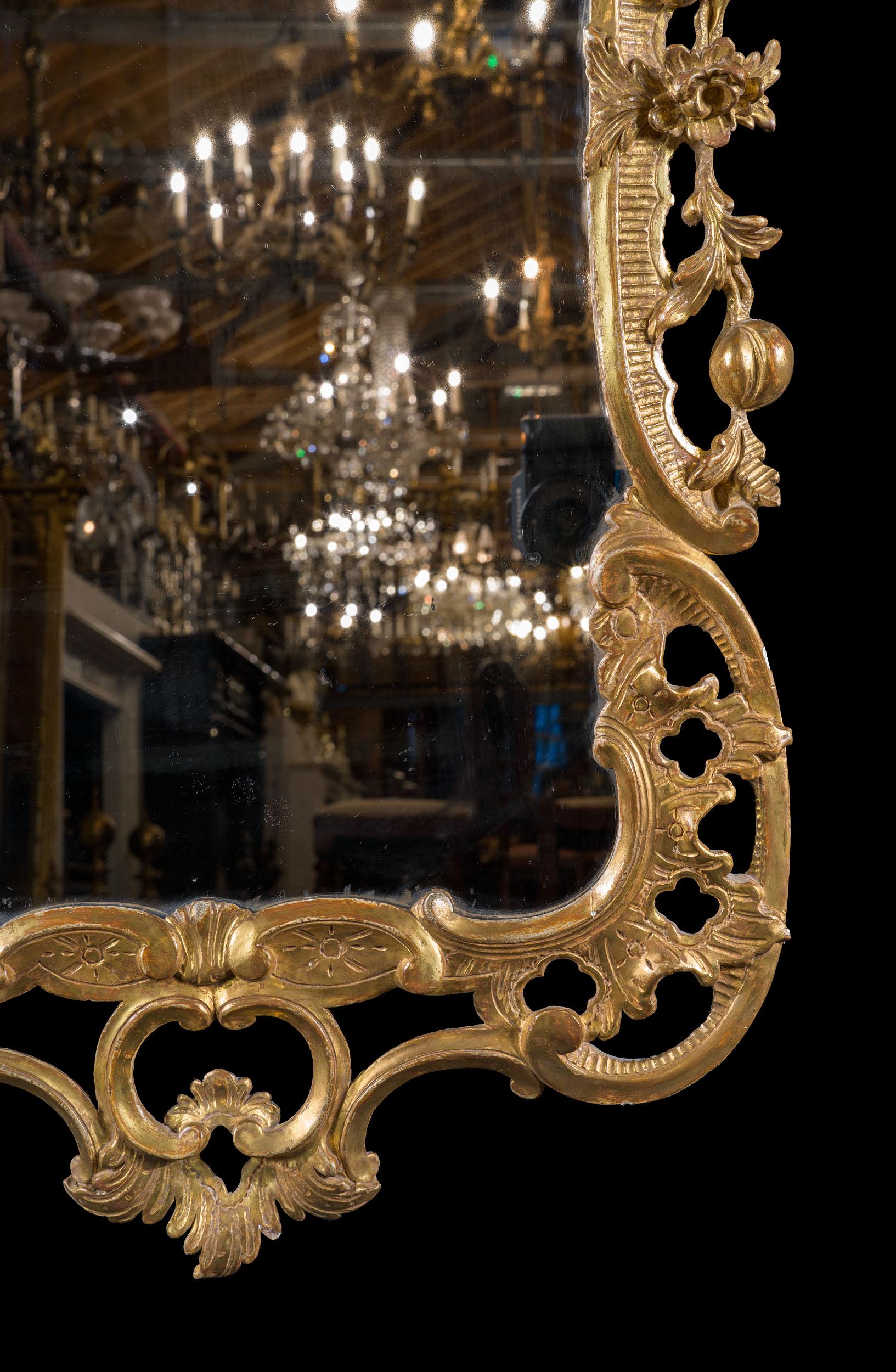 Miroir mural rococo en bois doré du XVIIIe siècle. Le cadre du miroir est sculpté avec assurance et finesse, avec des volutes, des fioritures acanthines et des fleurs en filigrane, motifs typiques du style rococo. La dorure est très belle et