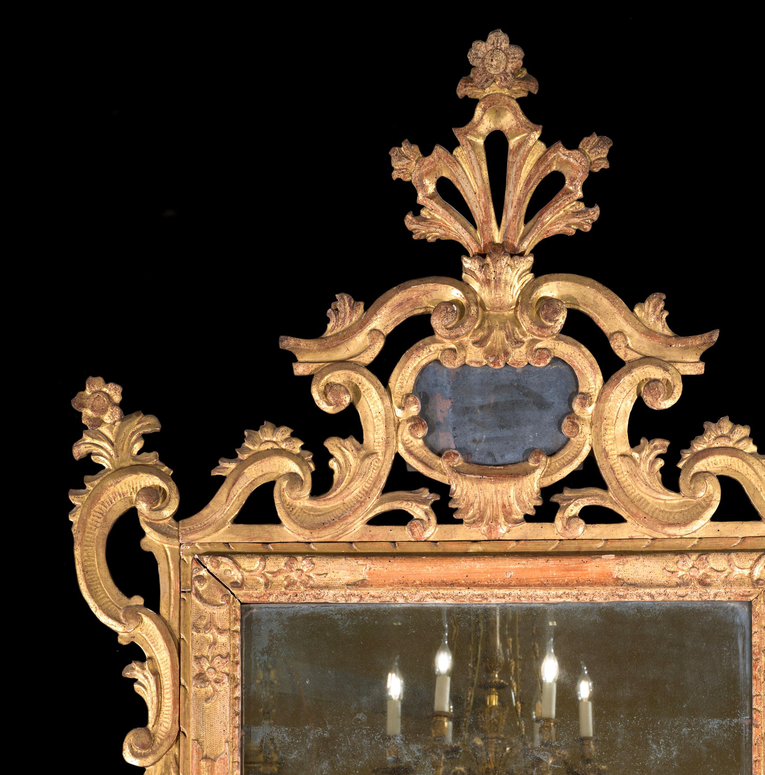 A fine mid-eighteenth century Venetian giltwood wall mirror. The elegant mirror is profusely decorated with foliate c scrolls in the Rococo manner, with floral flourishes and an elegant finial above an additional mirror plate. With original mercury
