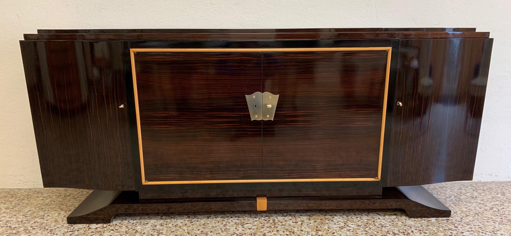 This precious sideboard was produced in France in the 1940s.
The sideboard is entirely covered in Macassar while the details are in solid maple and black lacquered.
The decoration on the central doors and the keys are made of brass.