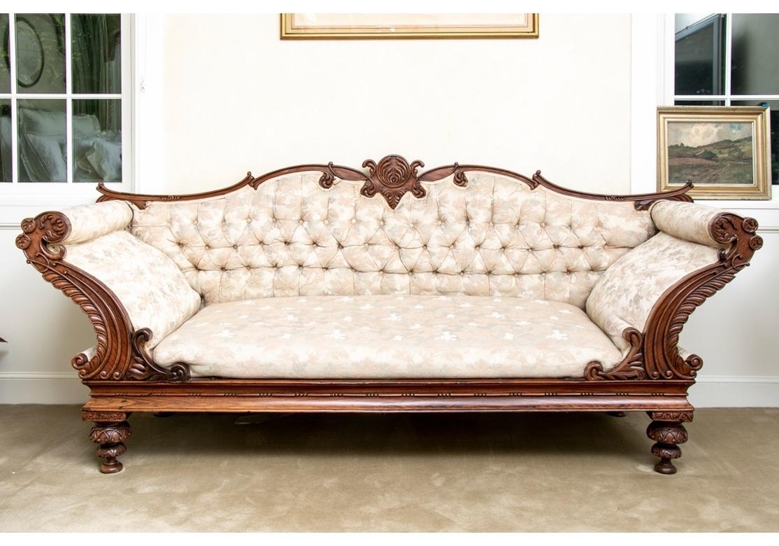 Sweeping Anglo-Indian carved frame sofa in grand dimension. Finely crafted with carved details overall. The serpentine crest rail with scrolls and center circular motif. The tall curved and rolled arms with rosettes and leafy edges. With a shaped