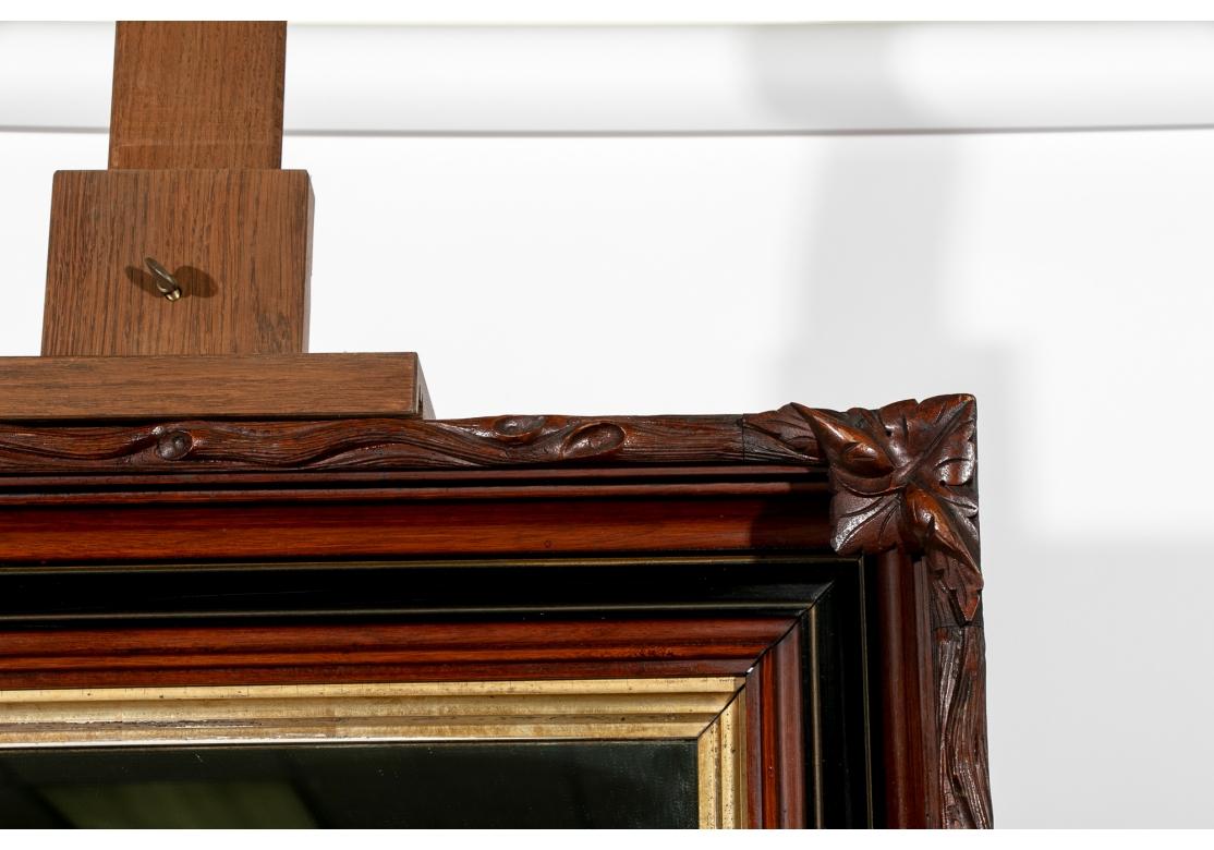 A deep mirror with a carved outer surround with sinuous tree branches ending in leafy corners. Several inner surrounds-  a curved mahogany band, a wide ebonized band, another carved mahogany band and an innermost gilt one.
39 1/2 x 33