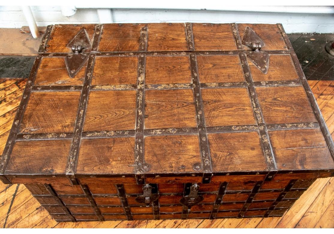 Possibly Near Eastern or Indian. A well-constructed Oak Trunk in a clear lacquered finish with many iron bands mounted in a criss-cross fashion, now suitable as a Rustic style cocktail table. The top with shaped iron mounts at the back for the