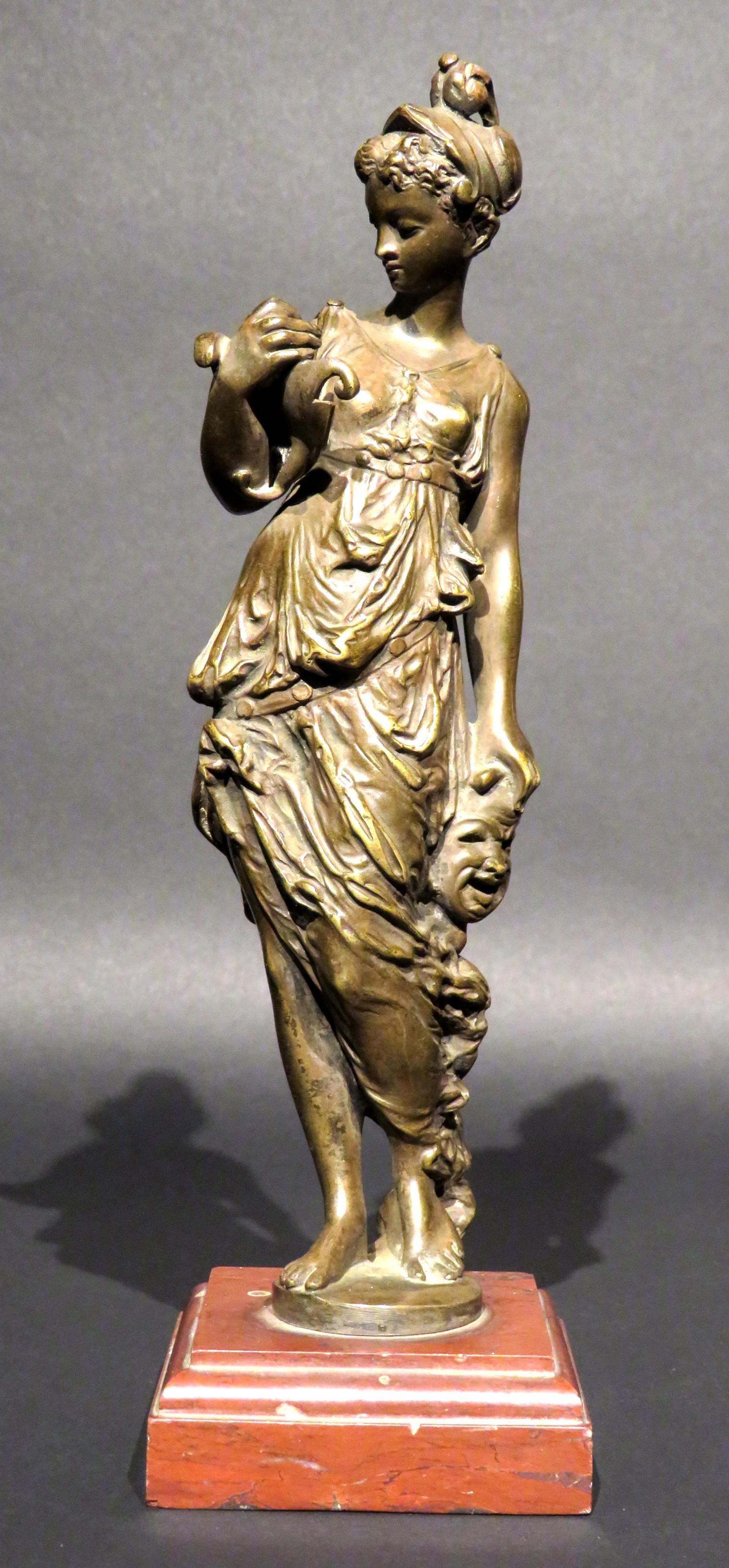 Die fein gegossene und patinierte Bronzefigur der Thalia, eine der neun griechischen Musen und bekannt als Göttin der Komödie und der idyllischen Poesie, steht in klassischer Kleidung und hält in der einen Hand eine komödiantische Maske und in der