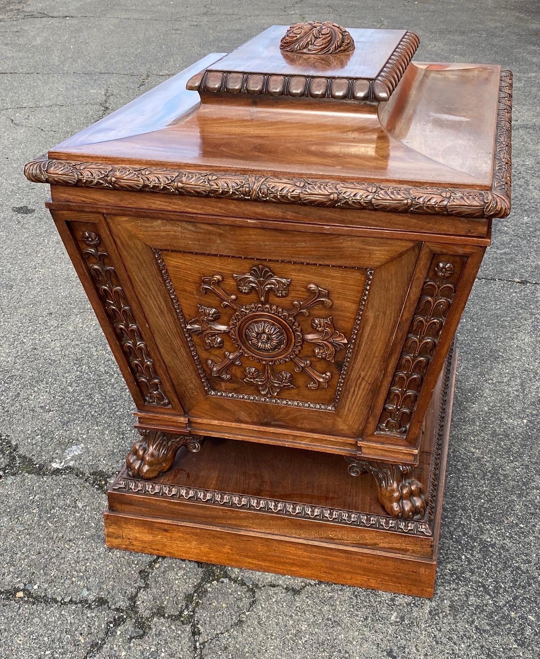 Fine 19th century English regency carved mahogany cellarette with pinwheel foliate finial, hinged lid, carved medallions, fitted interior, bracketed paw feet on a stepped base.