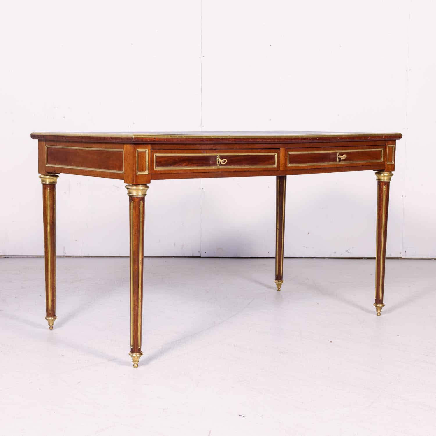 A fine 19th century French Louis XVI style bureau plat or desk handcrafted of mahogany by talented artisans near Lyon, circa 1880s. Having the original black tooled leather top above two drawers, this handsome desk features gilt brass trim and
