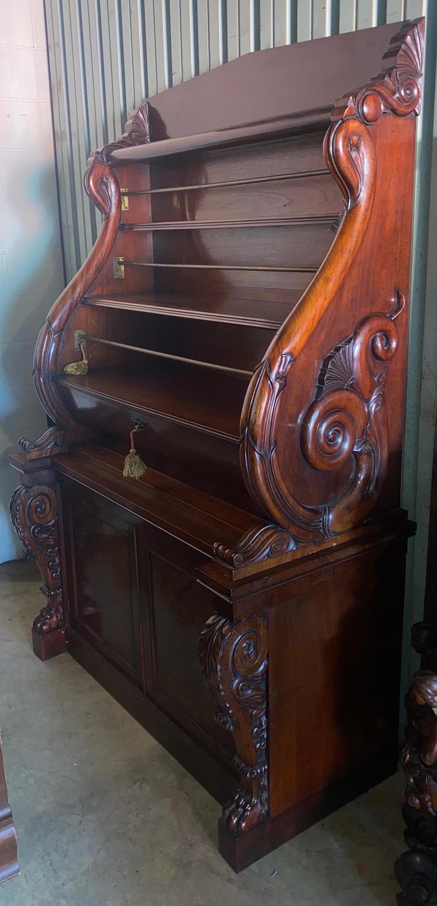 Raffinata libreria in mogano irlandese del XIX secolo con grandi volute intagliate, piedi a zampa, barre di chiusura, anta a quarto di tondo,