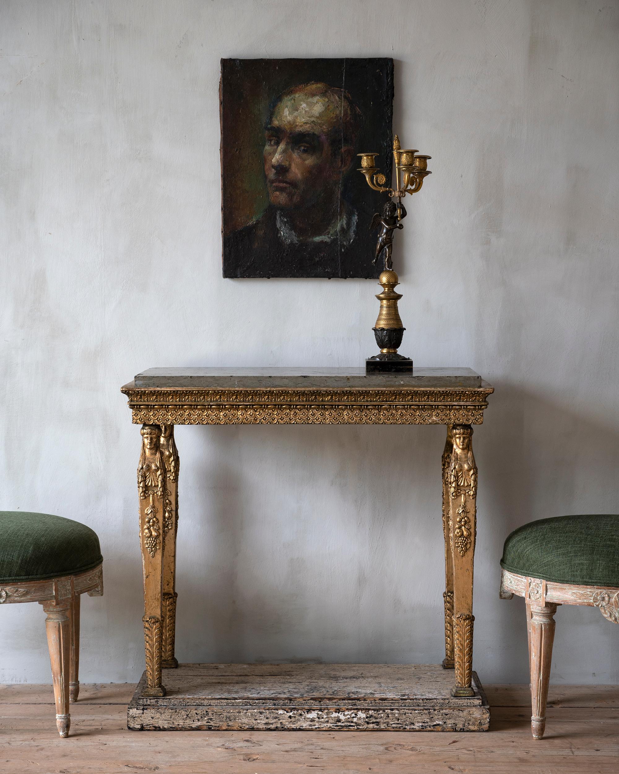 Table console en bois doré de la fin de la période gustavienne du 19e siècle. Sa pierre calcaire grise ciselée à la main est soutenue par quatre pieds fuselés en bois doré avec des figures féminines. Ca 1810 - 20 Stockholm, Suède. 