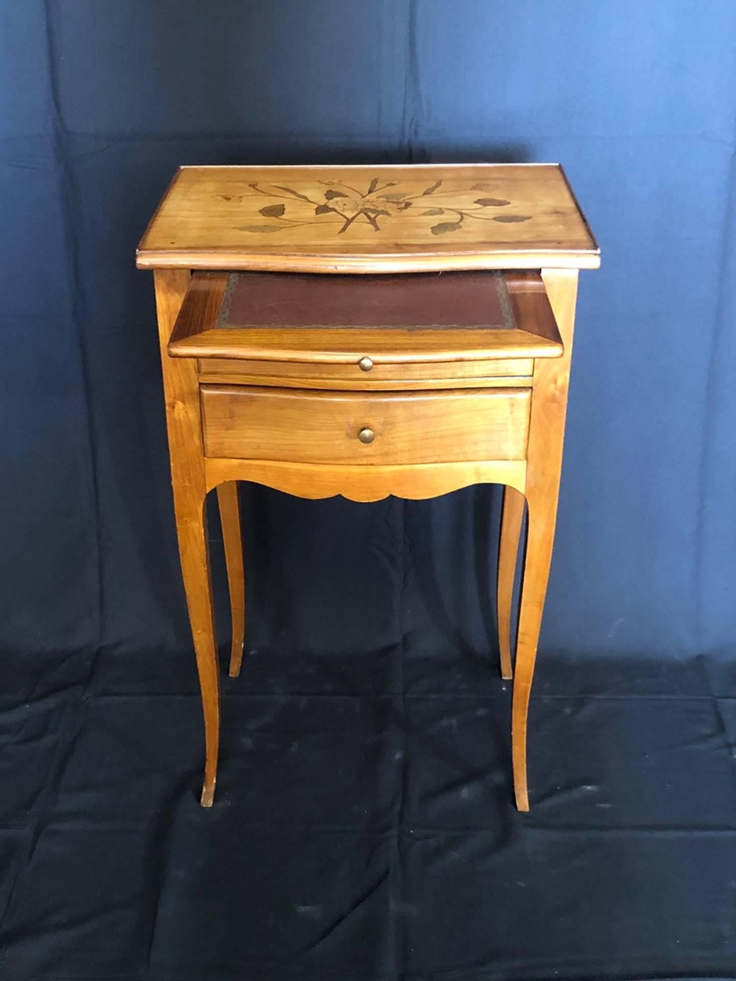 Beautiful French antique bedside nightstand cabinet having biscuit tones to the light walnut finish and lovely inlaid decoration and stylized flower marquetry on top. There are two beautiful doweled drawers and an embossed brown leather pullout /