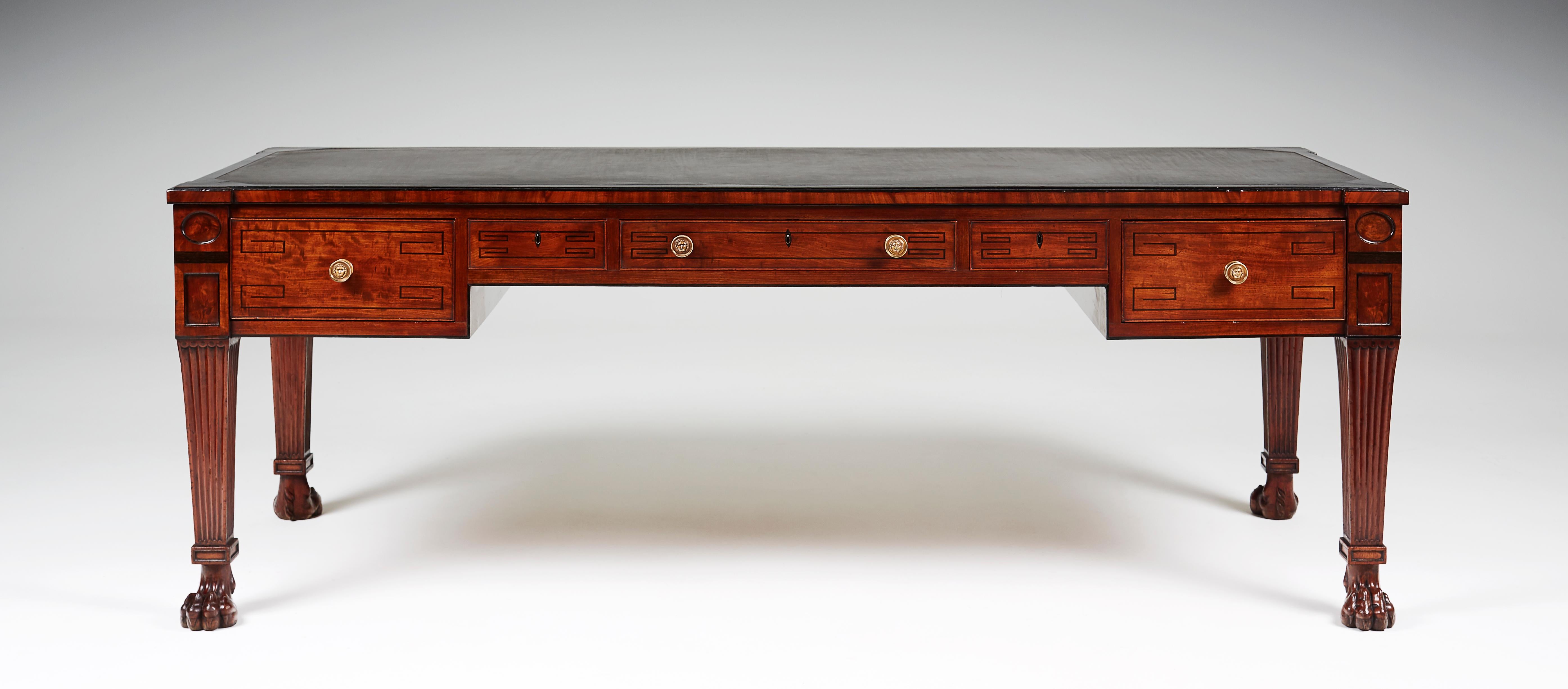 The long rectangular top with slightly outset square corners and inset with a slate slab, above a long and two short frieze drawers flanked by deep drawers, with dummy drawers opposing, raised on fluted square tapered legs ending in bold carved lion