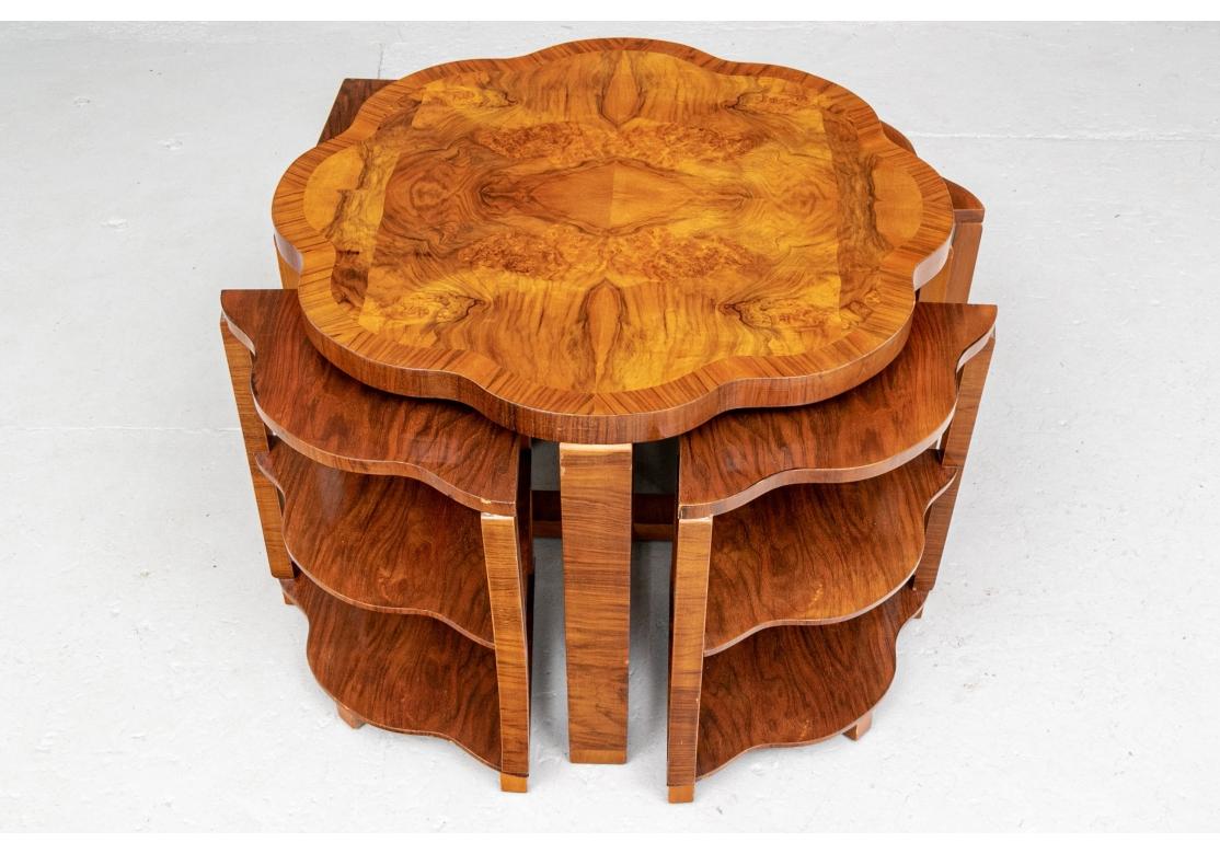 A fascinating and well made set of nesting tables in a truly original configuration. An end table in cross banded book matched figured wood. With a scalloped top, raised on square legs with X stretcher base. It encloses four triangular scalloped and