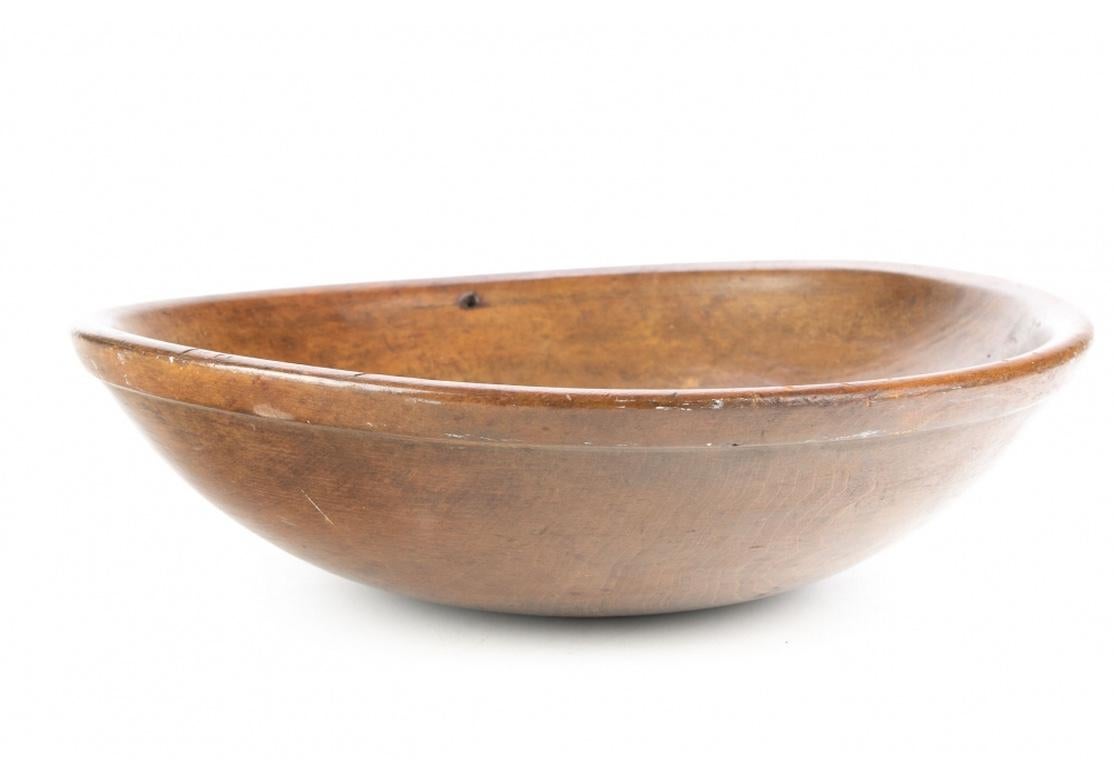 A large and well crafted turned wood bowl in a deep nutmeg stain with fine graining and very good condition. The finishing is fine with a very smooth and pleasing feel. The bowl has a well-defined .75” outer rim and there is a suspension hole just