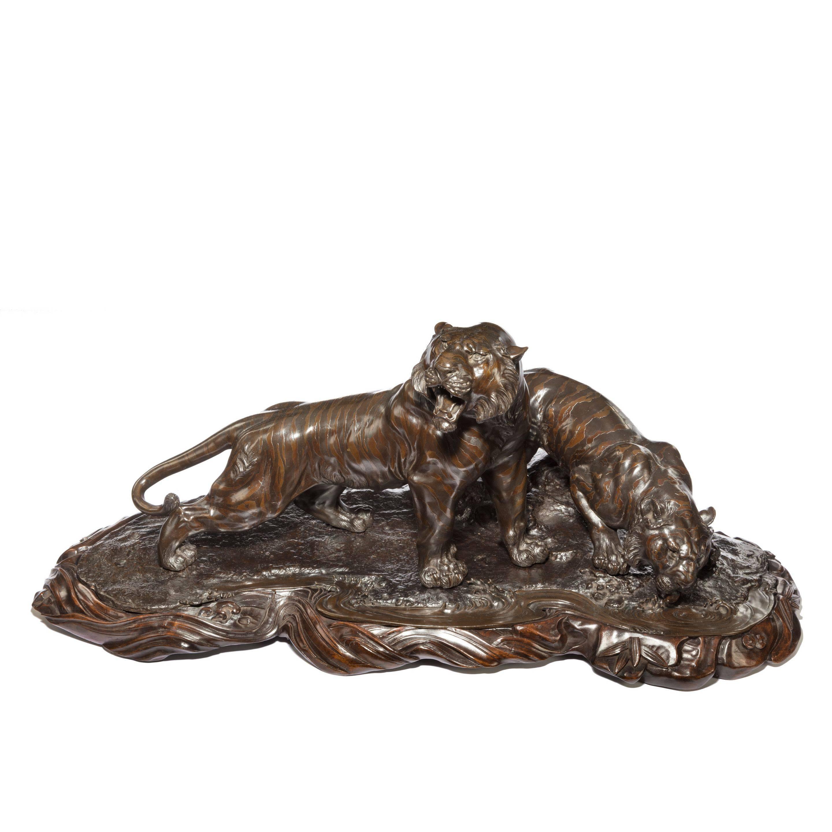 A fine and large Meiji period bronze of two tigers by Genryusai Seiya, the male standing alert on a rocky outcrop while the tigress laps from a puddle, naturalistically modelled and set into a carved hard wood base, the tigress signed with the seal