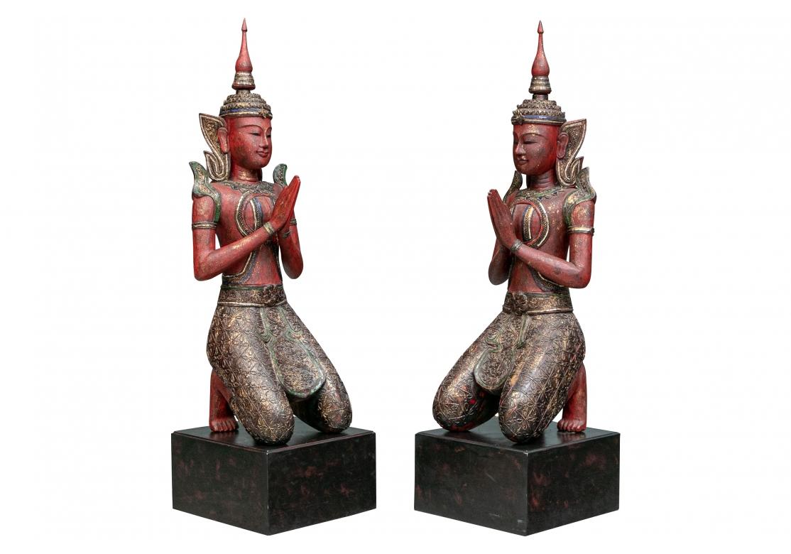 Paire de suppliants à genoux en bois sculpté, très décoratifs et sereins, peints en rouge vif moucheté d'or, avec des miroirs colorés appliqués dans des détails artistiques. Les paires sont originaires d'Asie du Sud-Est et probablement de Thaïlande