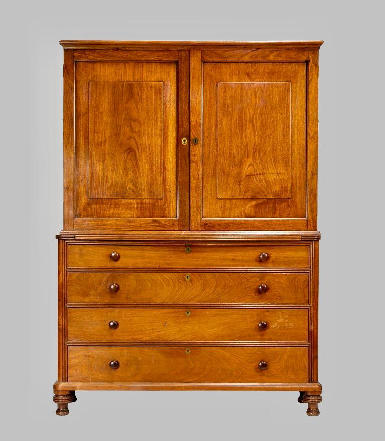 A fine and rare Anglo-Indian padouk wood cabinet on chest, the upper section with paneled doors opening to reveal 11 shelves lined in Fortuny style fabric over a central pull out shelf, the base fitted with 4 graduated drawers retaining their
