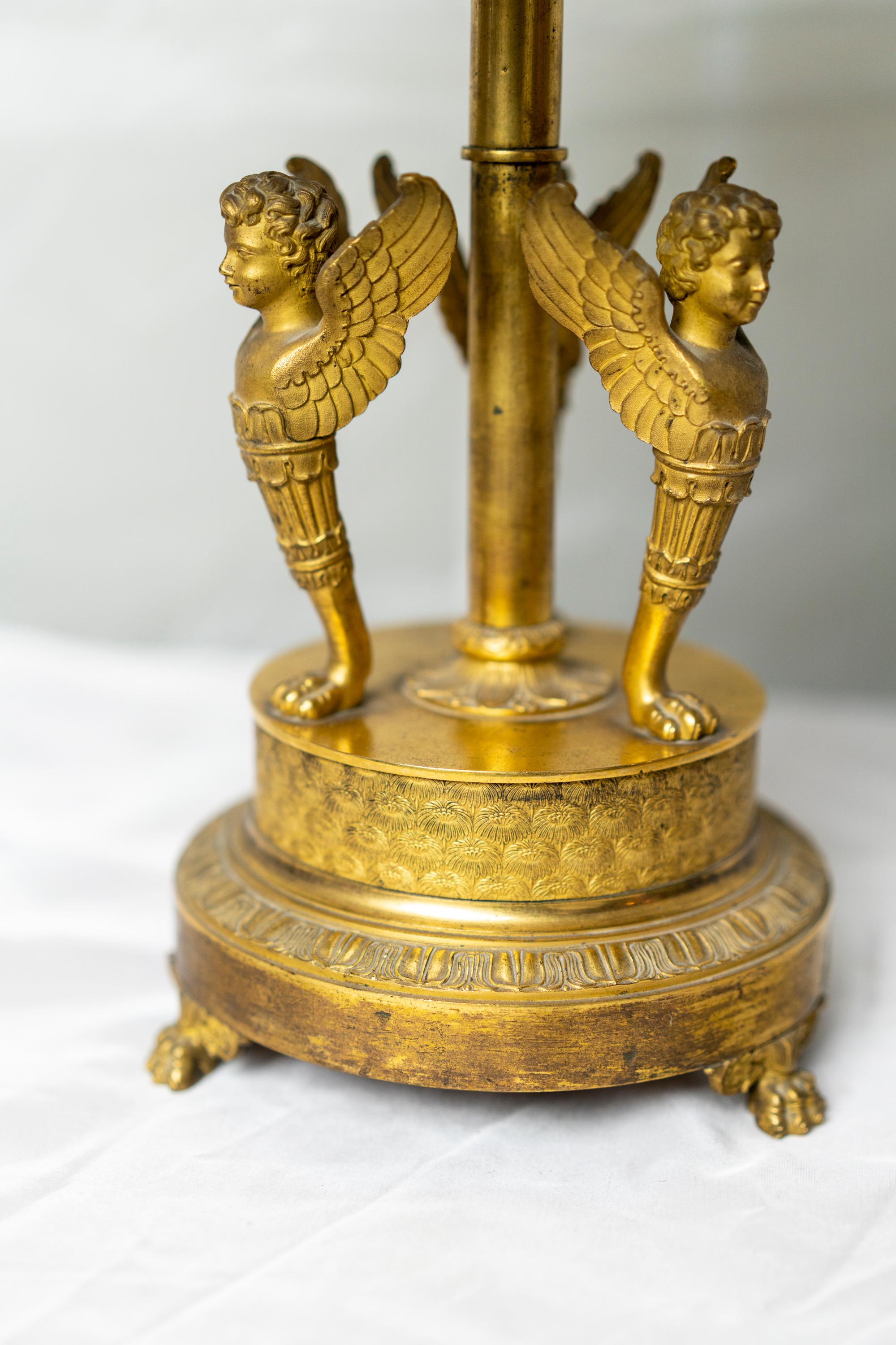 Belle et rare lampe de table bouillotte en bronze doré d'époque Empire avec des chérubins et décorée de palmiers en relief et reposant sur une base en pieds de pattes.
