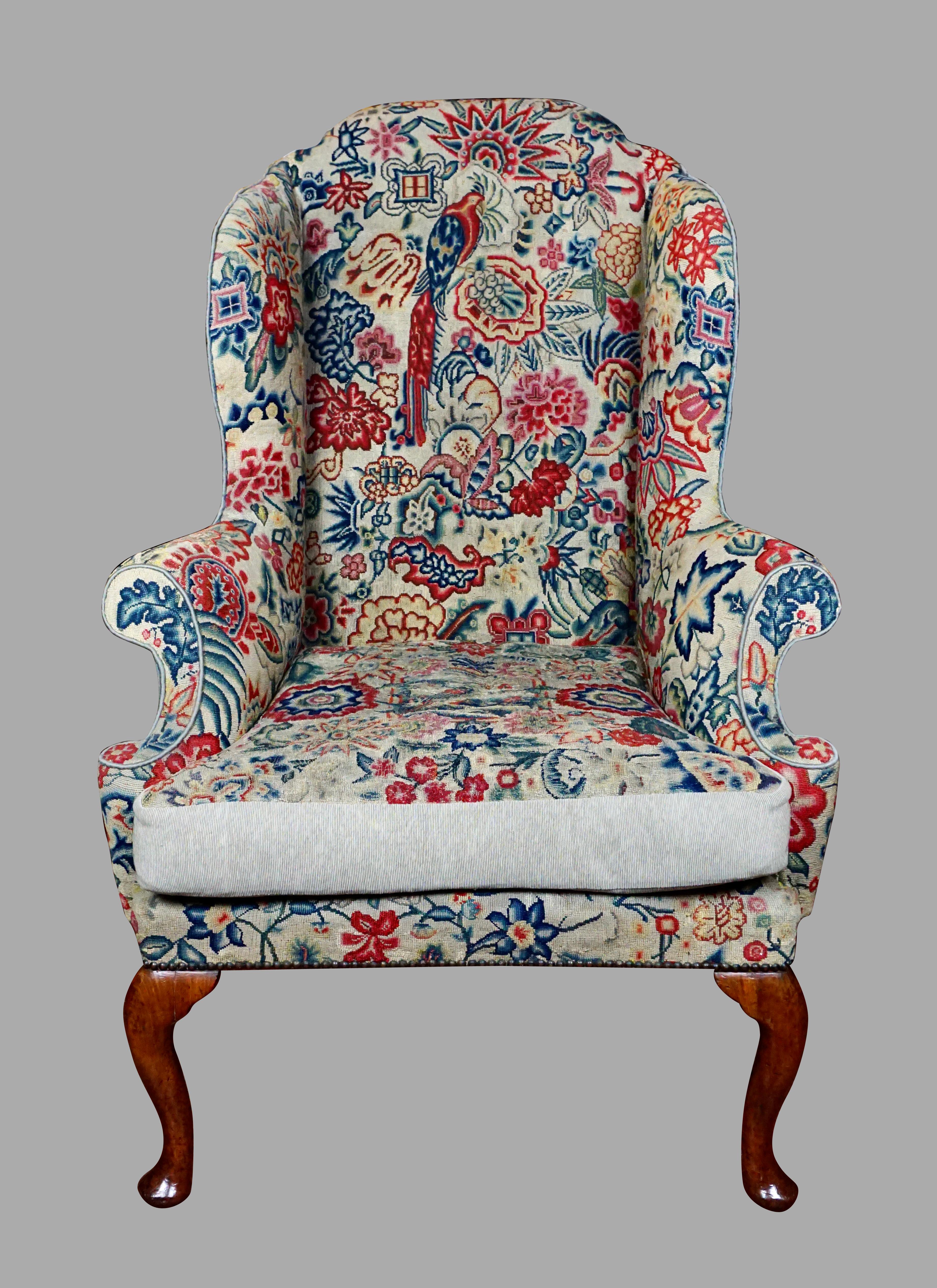 A good English George II period walnut wing armchair with cushion, upholstered in gros and petit needlepoint material, the chair dating from the early part of the 18th century. The needlepoint depicts an exotic bird in a stylized overall floral