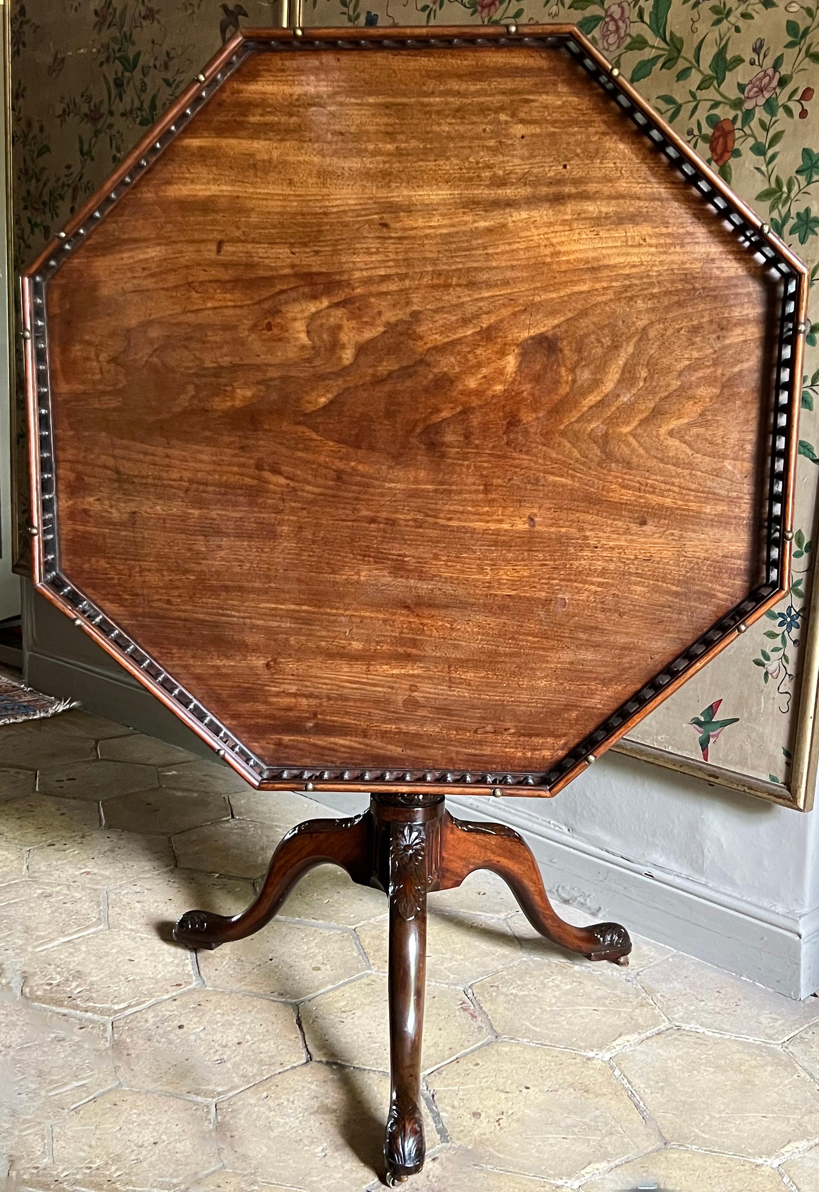 This fine, larger than usual, George ll-period table has a baluster-galleried octagonal top supported on a birdcage, allowing the top to both swivel and tilt. Note the fine, tapering, fluted column continuing into a carved collar. The well-drawn