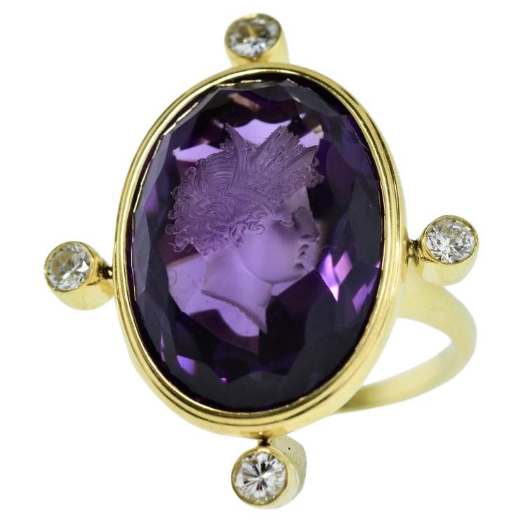 L'améthyste sculptée antique pesant environ 20 cts présente une belle couleur violette profonde et claire. Cette intaille ancienne, datant de 1875, a été montée sur une bague contemporaine en or jaune rehaussée de diamants aux points cardinaux. Les