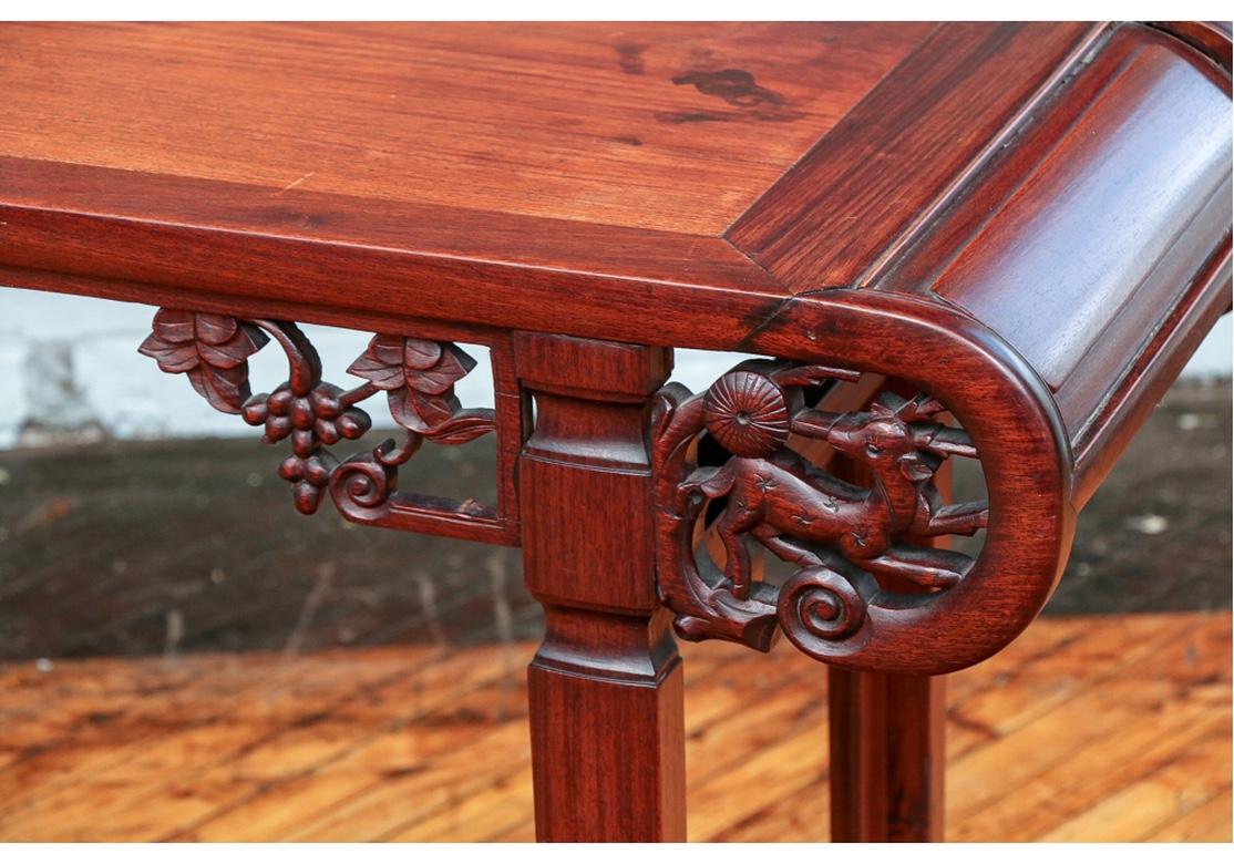Fine antique Asian carved rosewood scholar’s table a scholar’s table with handsome wood, excellent form and handsome contrasting woods. The banded top mounted on a scrolled frieze with carved openwork grape clusters and deer. Raised on shaped