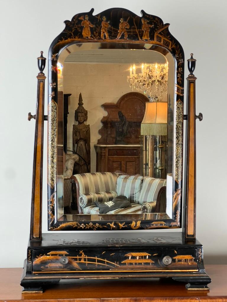 A striking late 19th century Chinoiserie black lacquer dressing mirror, this fine example is as much an art object as it is a functional piece. The frame is adorned with delicately hand-painted gilt figural scenes and architectural motifs across the