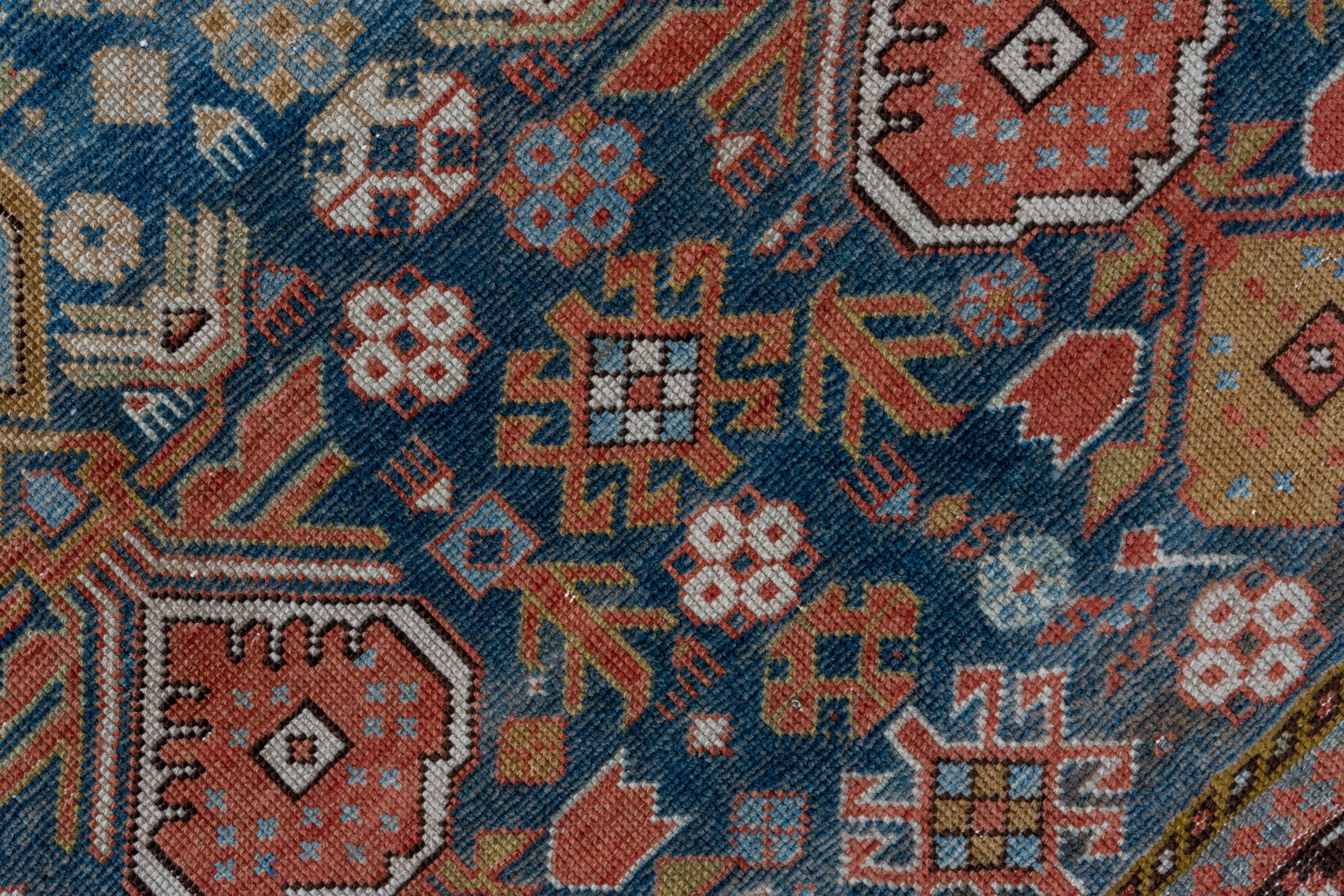 The abrashed slate blue field shows an ascending, one-way, two column pattern of six connected shield palmettes each, in pale blue, coral, rust and ecru. Hooked diamond secondaries. Eggshell border with a tendril and geometric blossoms.
