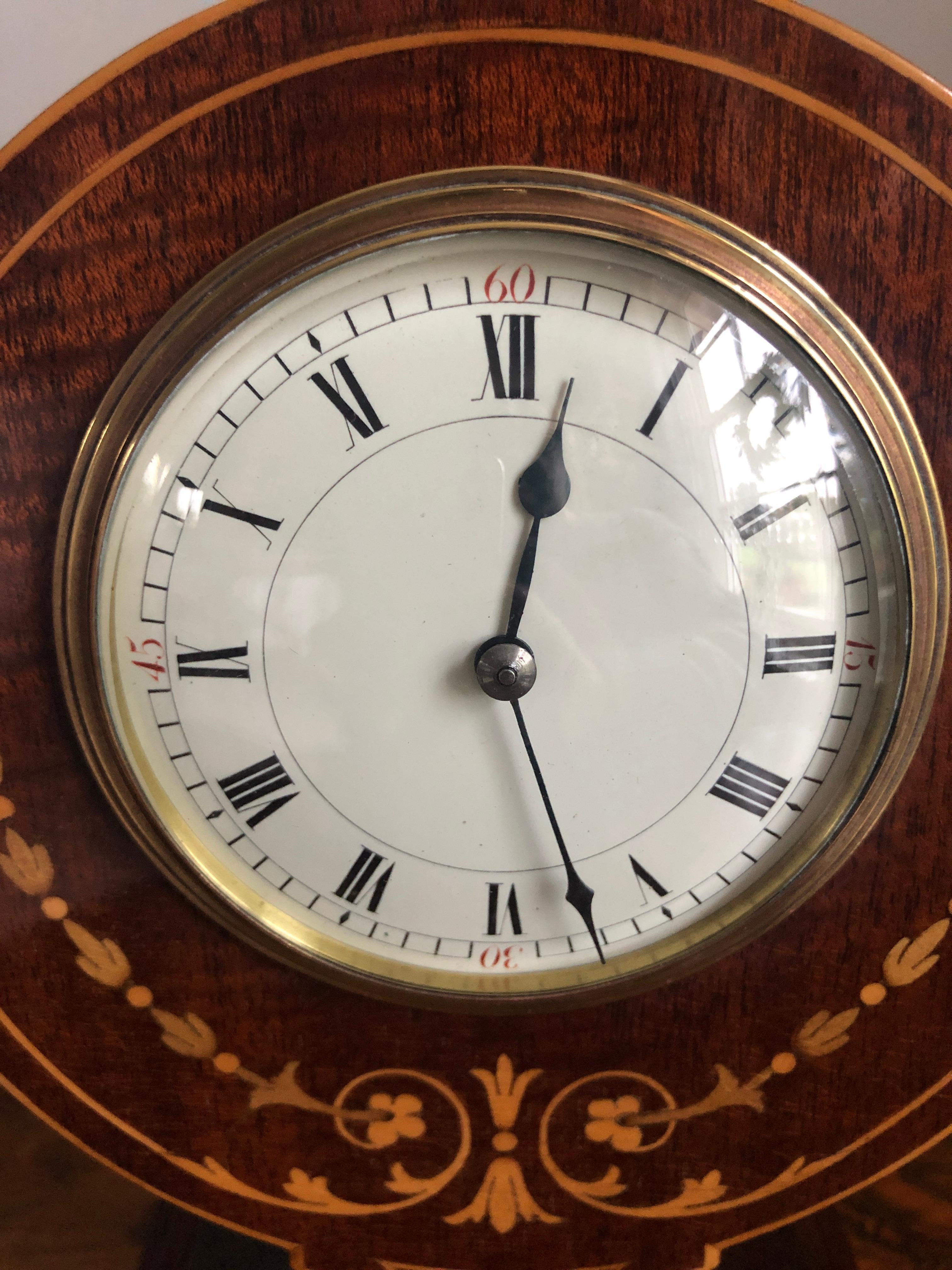 Fine Edwardian inlaid mahogany desk clock having a magnificent inlaid balloon shaped marquetry case with original brass ball feet. An elegant enameled dial with original hands with an 8 day movement. It is in good working order and comes with its