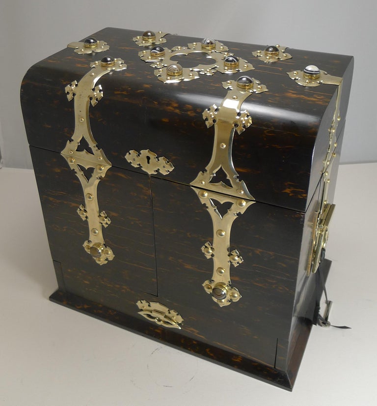 A truly magnificent drinks / decanter box made from exotic Coromandel mounted with polished brass mounts inset with a plethora of different kinds of cabochon cut and polished onyx stones.

I would expect the box to made by the top-notch G