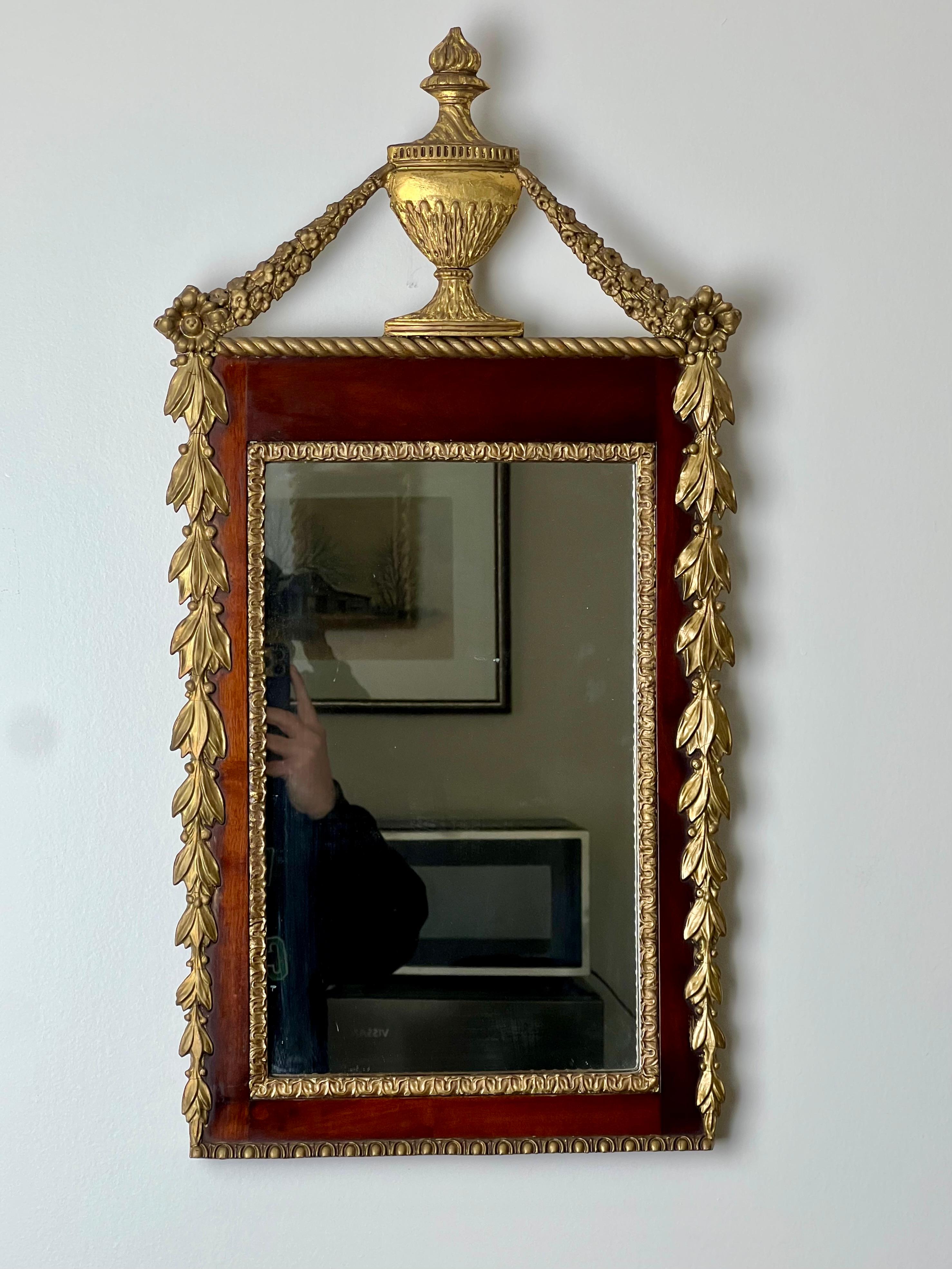 Este fino espejo de pared dorado de época federal, datado hacia 1830, encarna la elegancia y la sobria belleza características del estilo federal. El espejo tiene un marco de caoba finamente trabajado, realzado con un delicado dorado a la parcela.