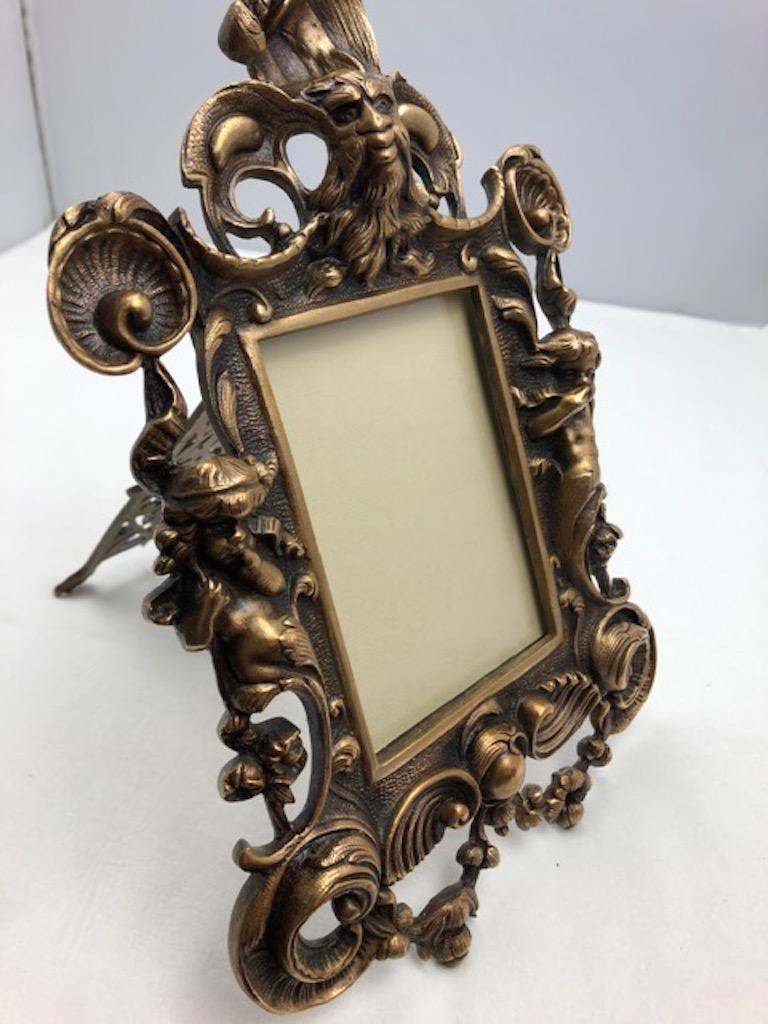 A fine ornate antique French Louis XV style gilt bronze photo frame with back easel stand, Napoleon III era, circa 1880. Richly decorated with neoclassical style motifs such as faces of goddesses, cherubs, and winged man figures, France.

Perfect