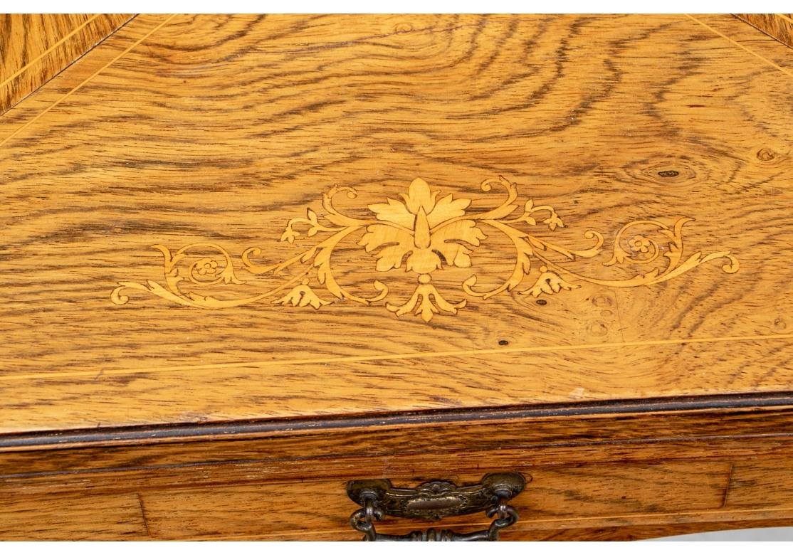 A small square games table in figured oak with foliate marquetry on the four sides and fine string inlays. The frieze with scrolled lower edge and one small drawer. The hinged sections opening to a figured wood gaming surface with pale wood circular