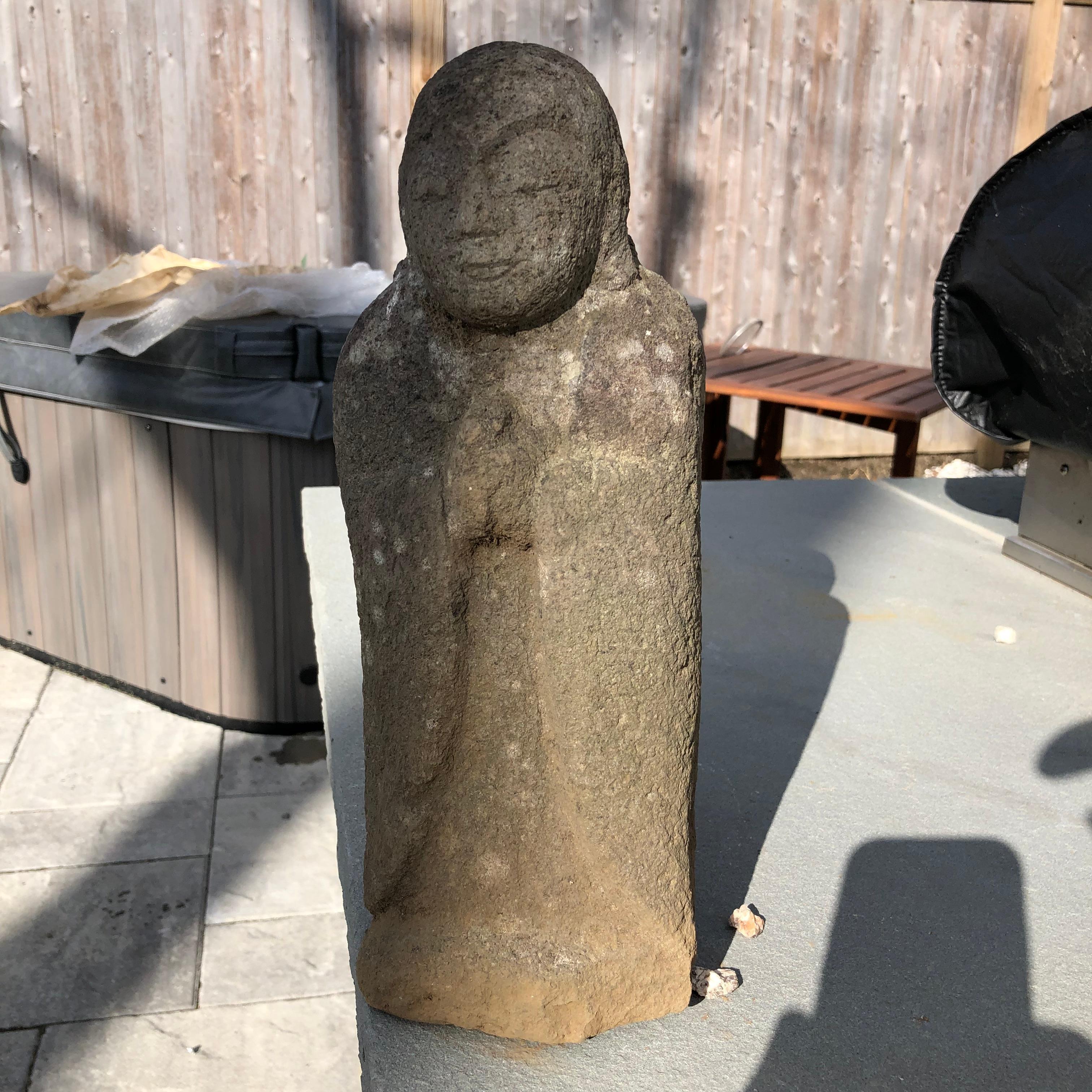 A fine, beautiful and uncommon style Japanese Standing Buddhist stone Jizo Bosatsu stands tall clutching his hands in 
 the gassho mudra of adoration. This handsome example is figurally sculpted from tuff, an igneous stone composed primarily of