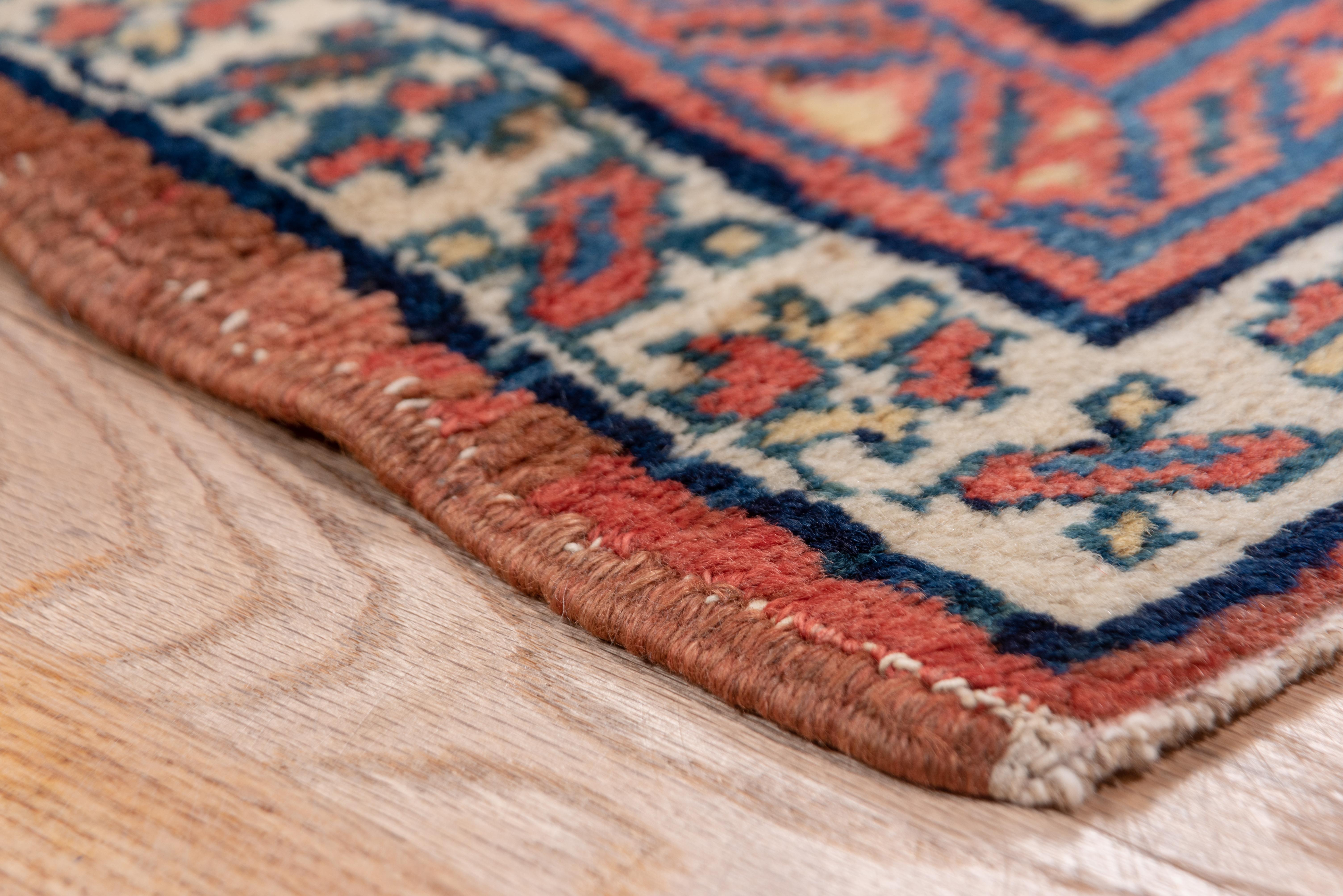 This attractive runner from someplace in Azerbaijan province shows a bright red tone ground with seven detached escutcheon medallions in shades of medium blue, with zig-zag bands flowing around them. Reversing triangle main border, and matching star