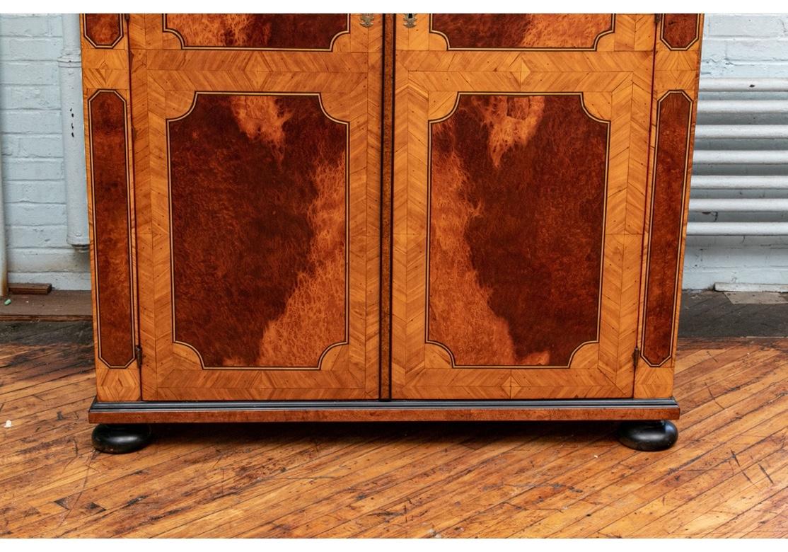 A finely crafted armoire with parquetry banded double doors and sides inlaid with matching shaped burled panels. Brass escutcheons with a key. The carved cornice with ebonized moldings and raised on ebonized bun feet.
The doors open to reveal a