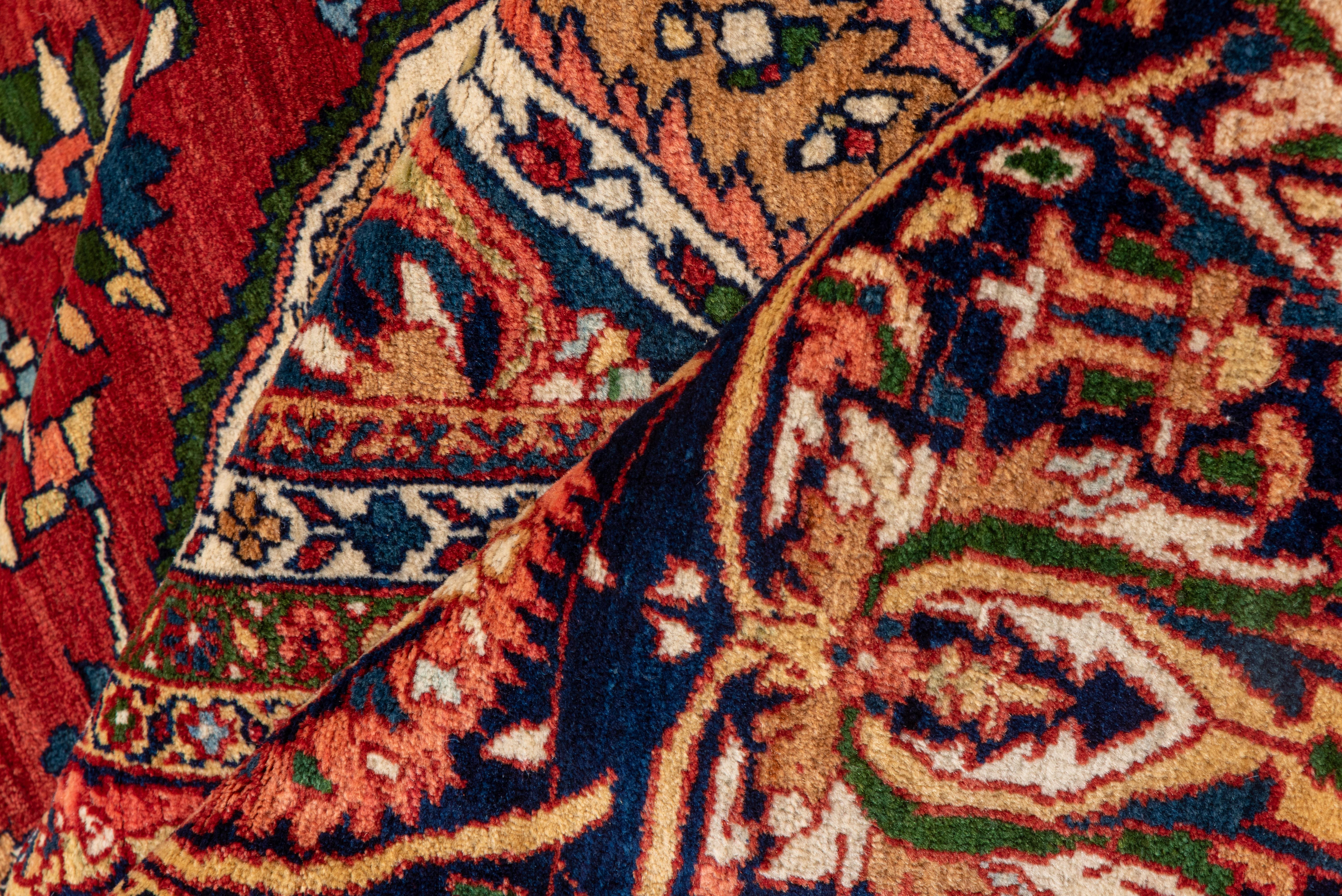 This palace-sized west Persian finely woven village carpet shows a crisp ruby-red field, cerulean blue medallion and ivory corners, all with small both detailing everywhere. Dark blue main border with emphatic C-shaped leaves presenting pink and